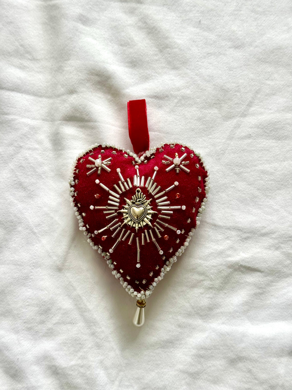 Decorative heart ornament with red fabric and silver embroidery on a white textured background