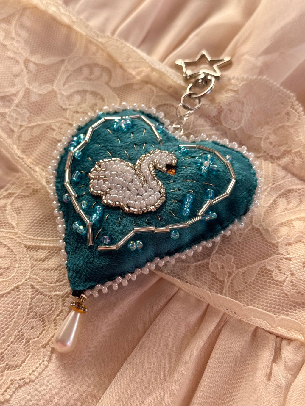 Decorative heart-shaped brooch with a swan design on a textured fabric background