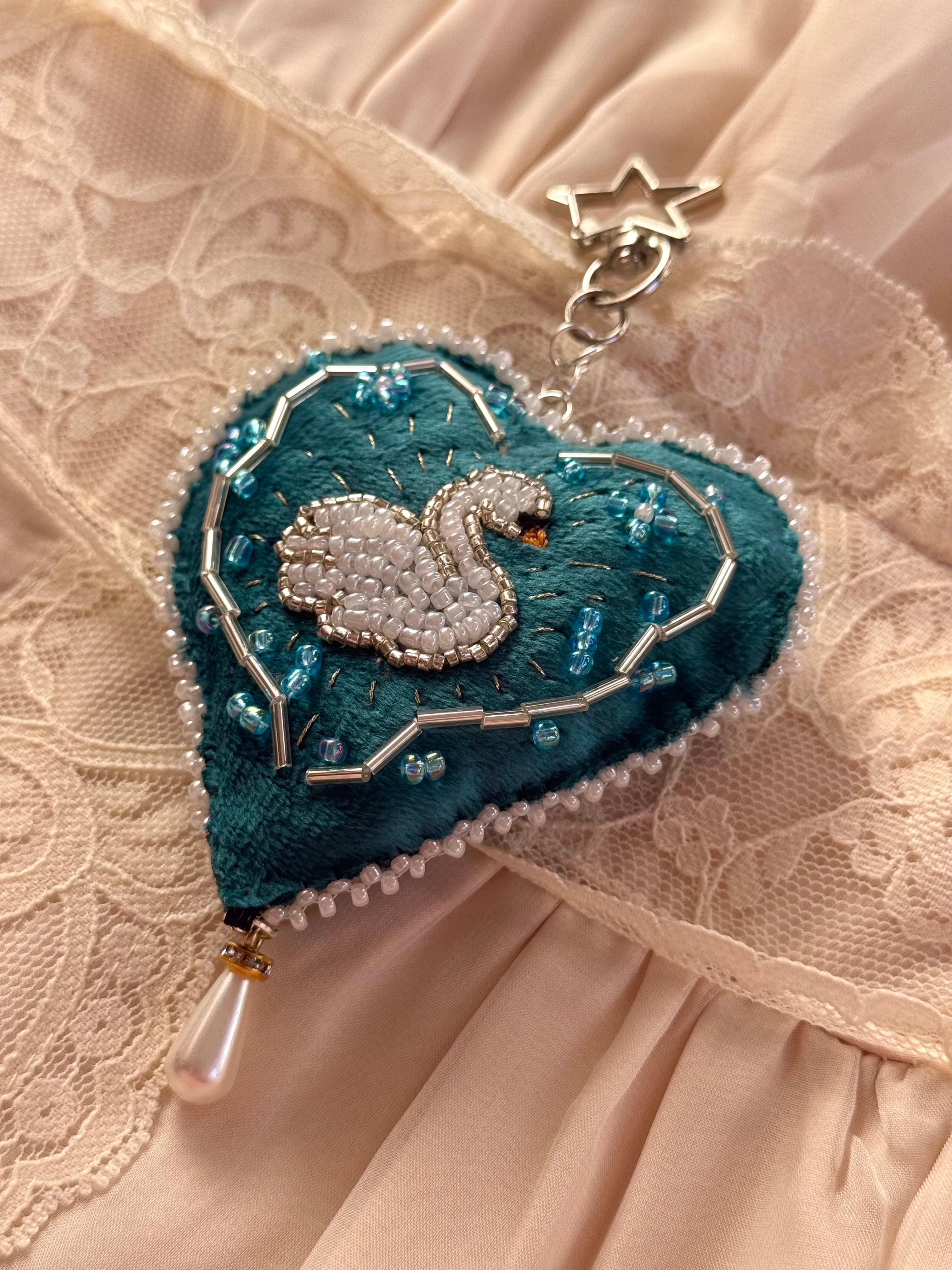Decorative heart-shaped brooch with a swan design on a textured fabric background