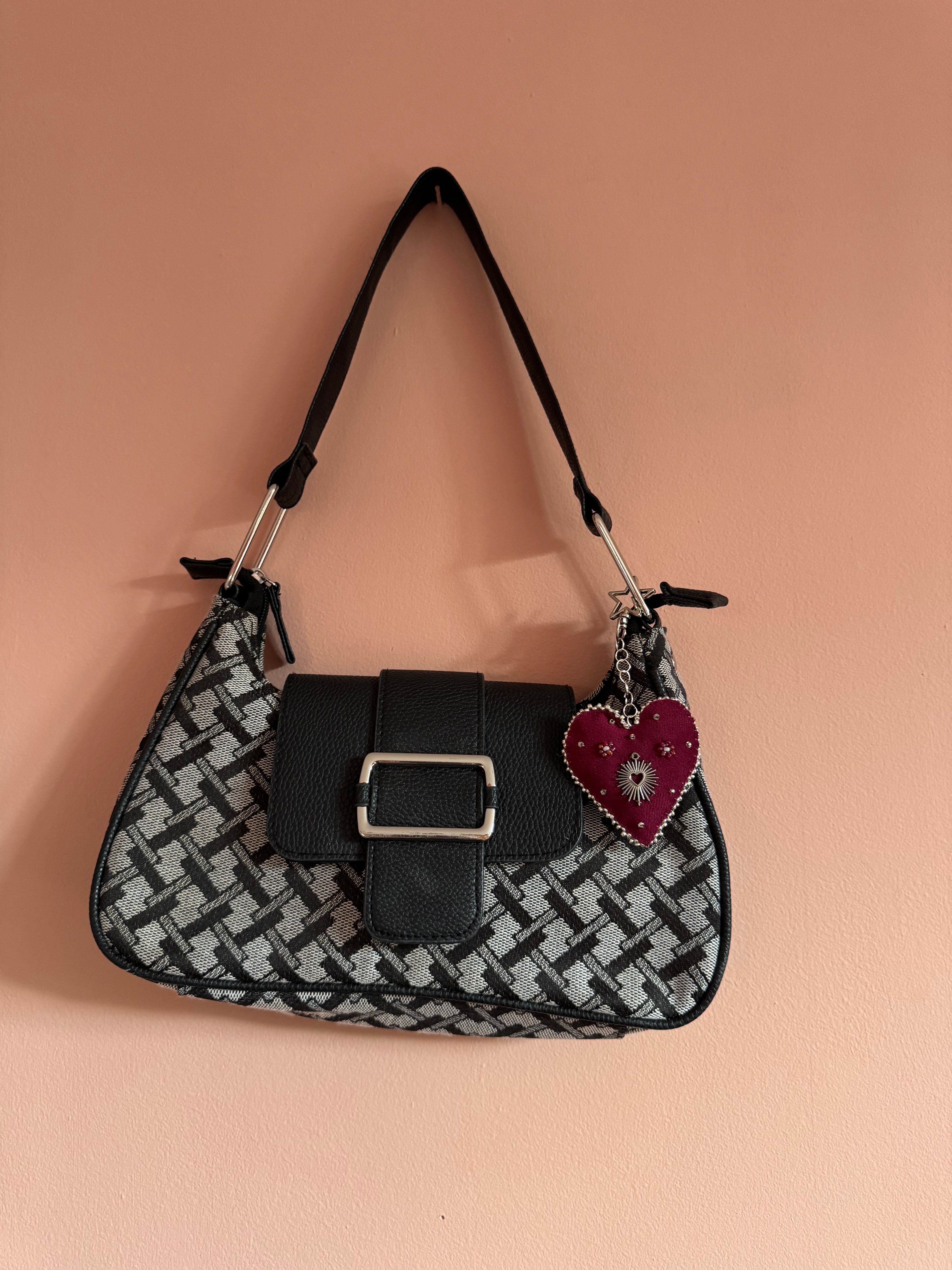 Black and white patterned bag with a heart-shaped charm on a beige background