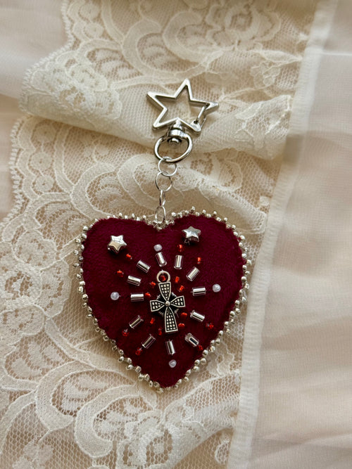 Heart-shaped embroidered pendant keychain with star and cross designs on a lace background