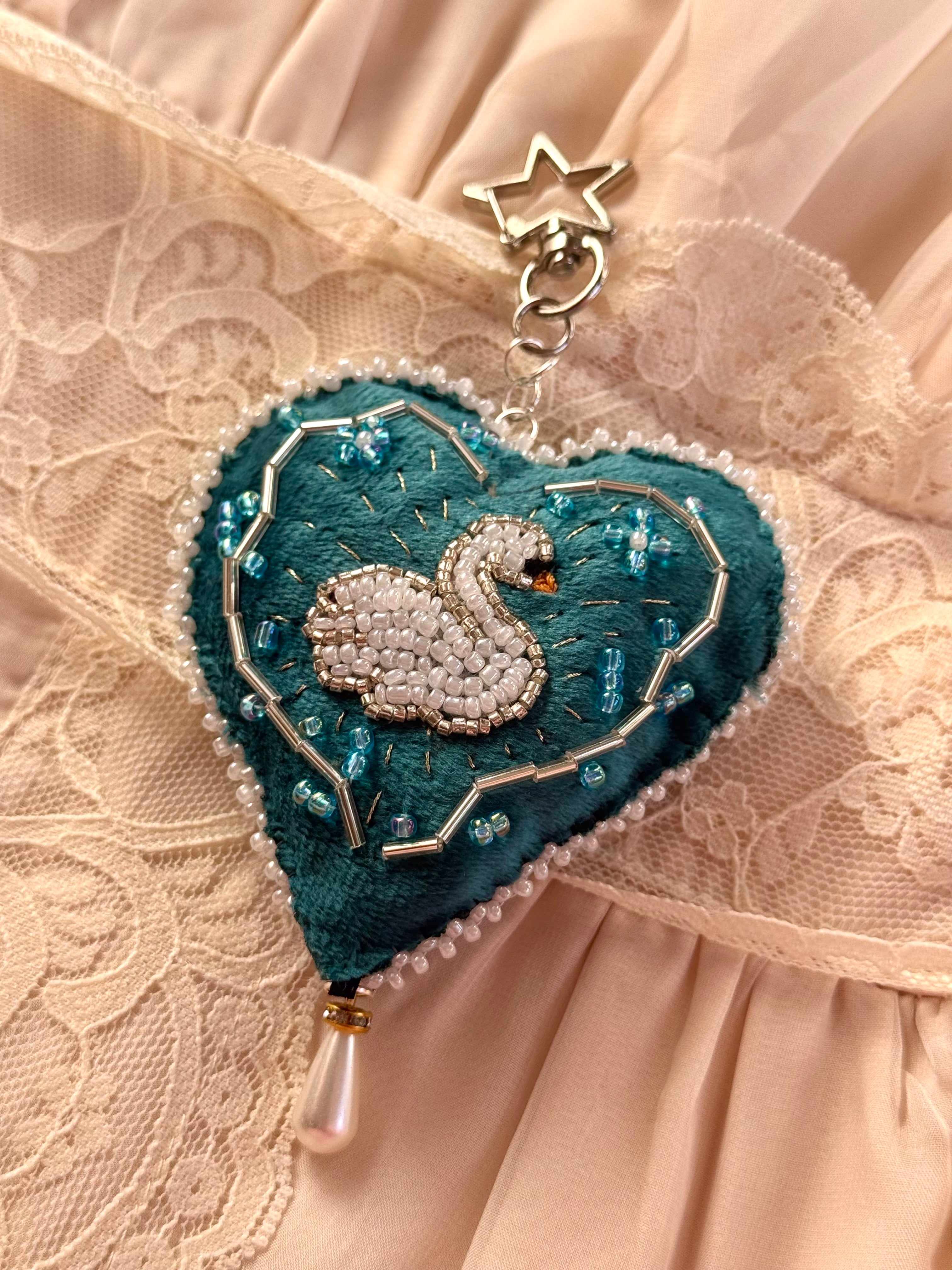Heart-shaped brooch with swan design on a lace background