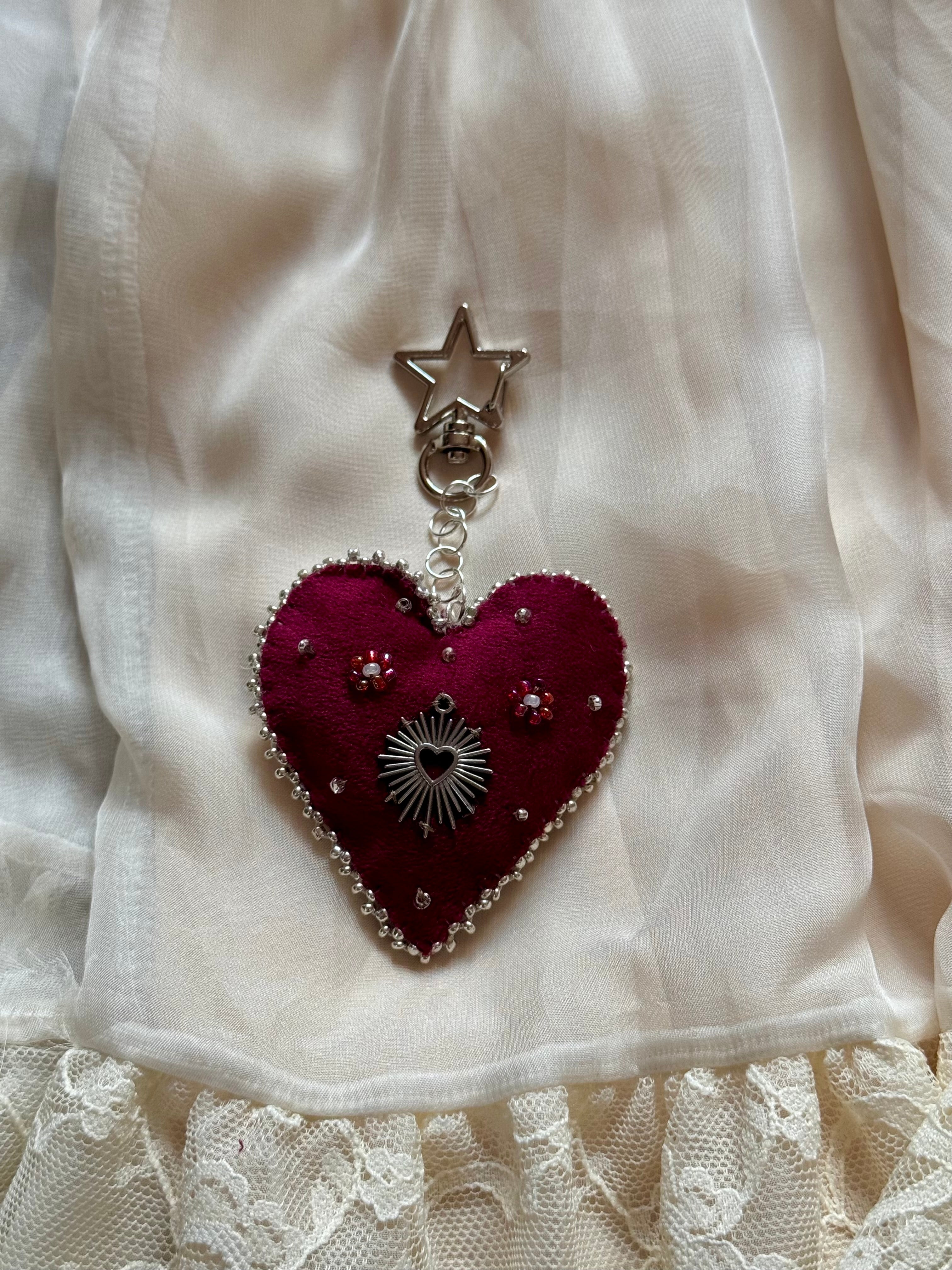 Heart-shaped brooch with star and sun design on a white fabric background