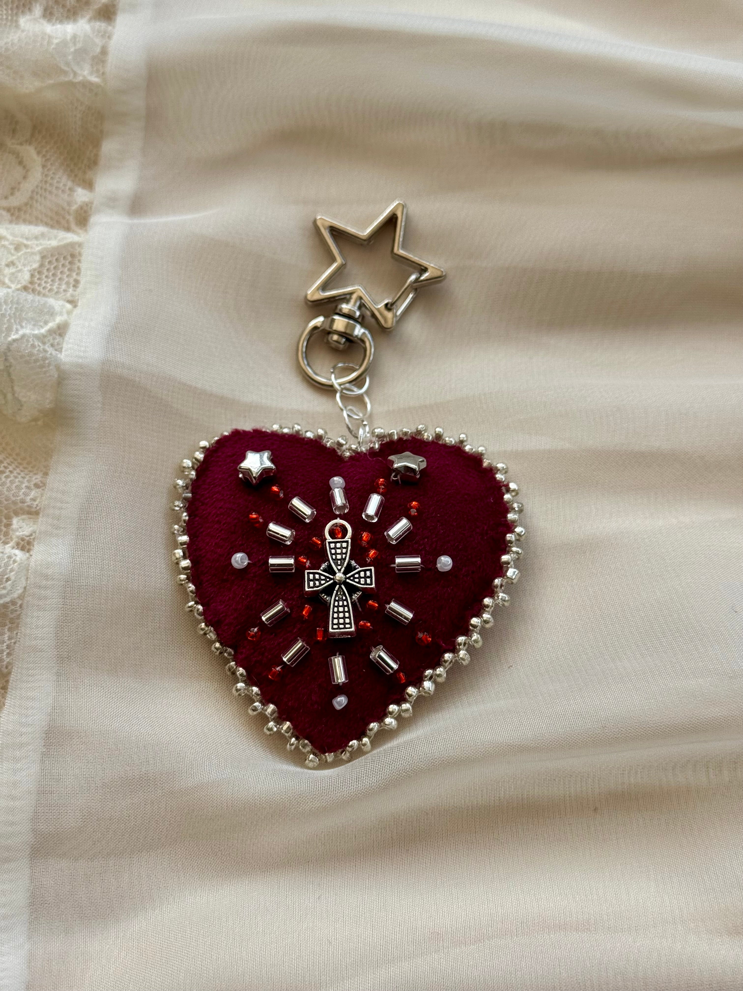 Heart-shaped embroidered pendant keychain with star and cross designs on a lace background
