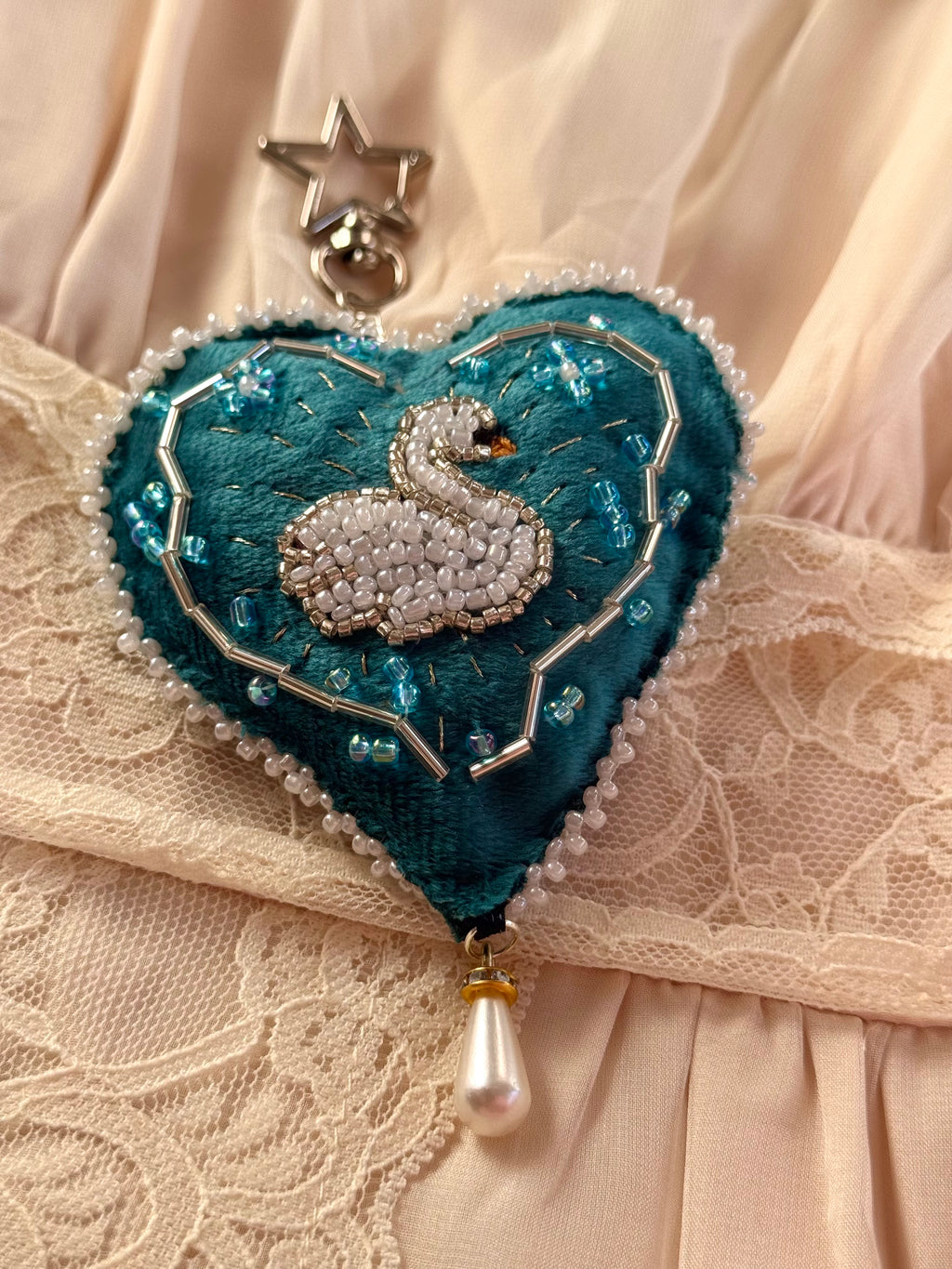 Heart-shaped brooch with a swan design on a lace background