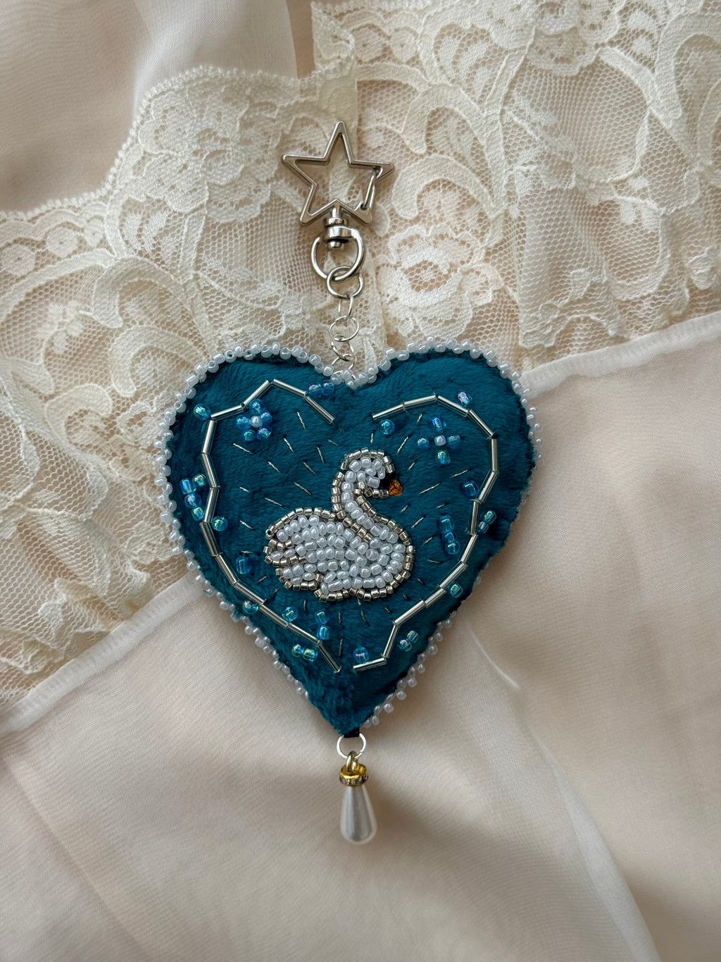Heart-shaped embroidered pendant with a swan design on a lace background
