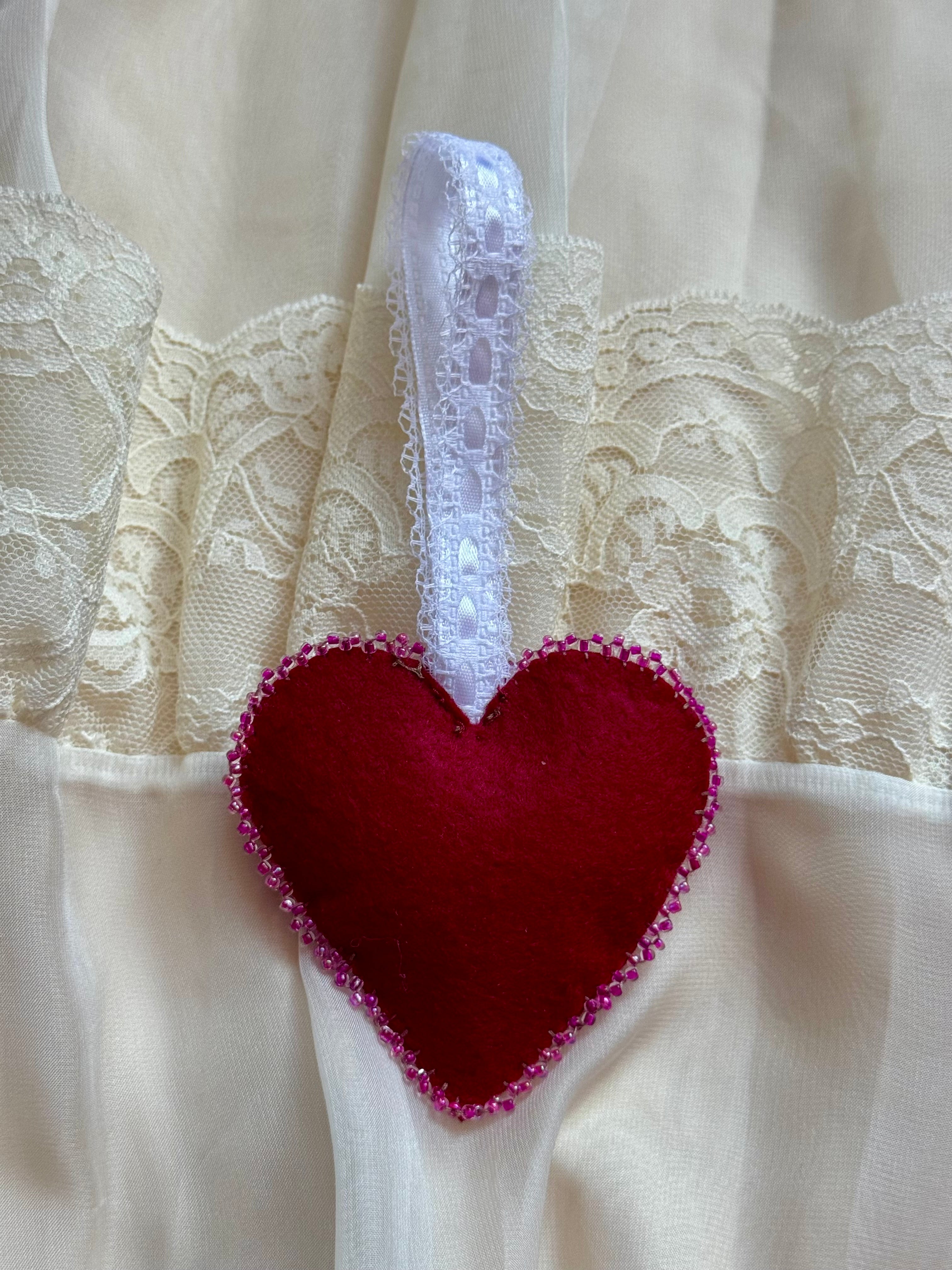 Red heart-shaped decorative item with a white lace handle on a lace background