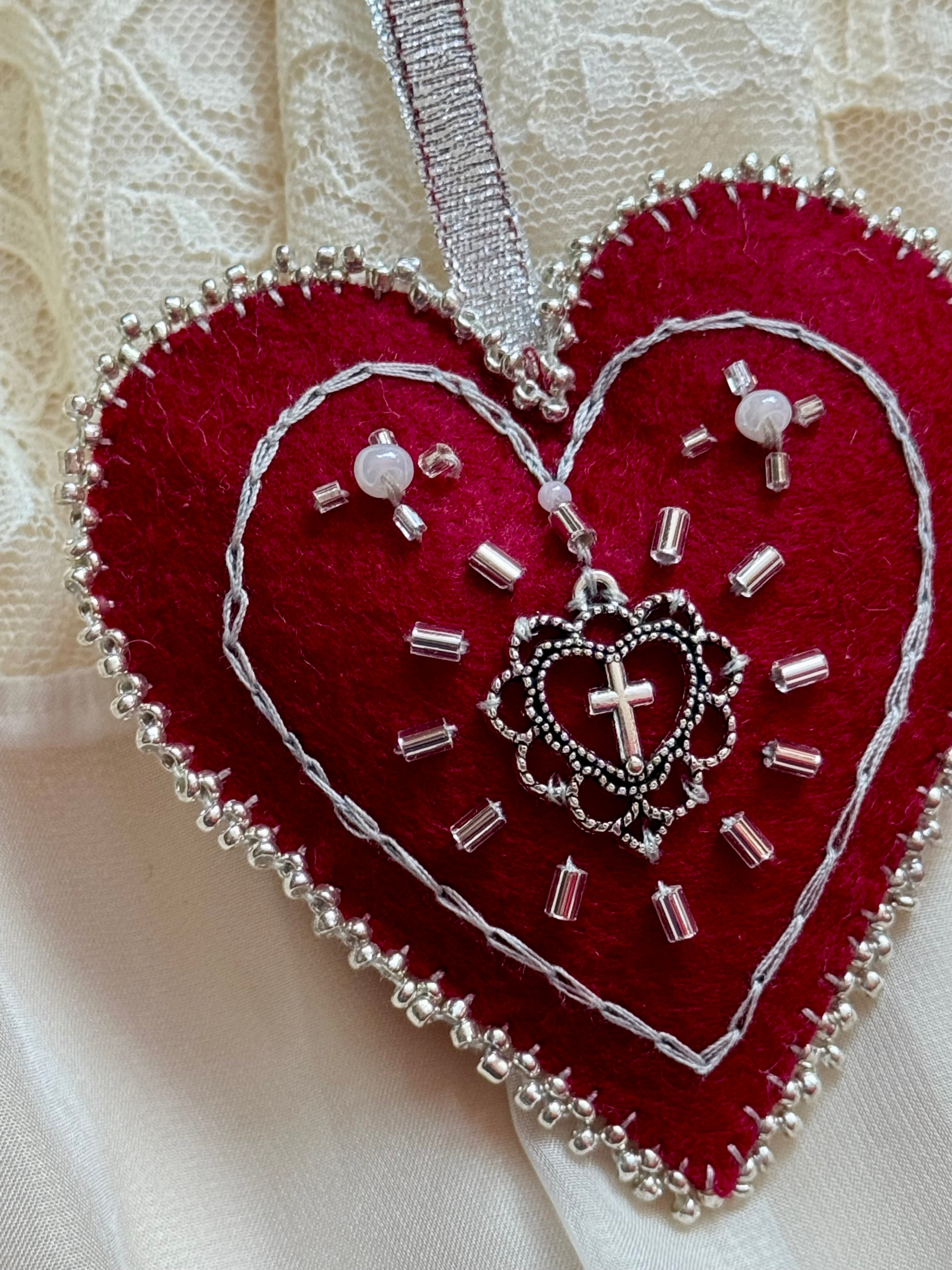 Heart-shaped embroidered decoration with beads and a cross on a white lace background