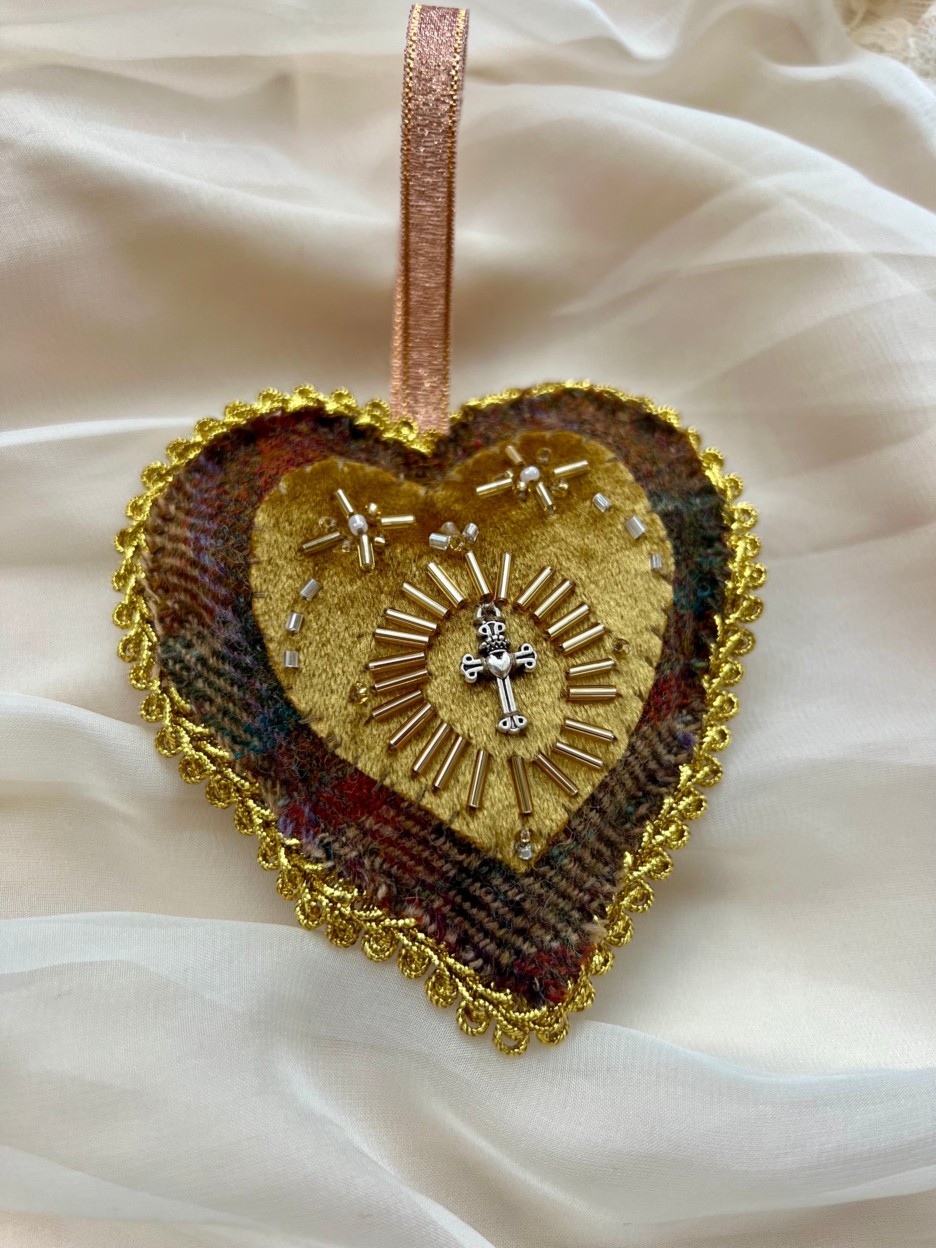 Decorative heart ornament with gold detailing and a cross on a white fabric background