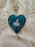 Decorative heart-shaped pendant with a swan design on a lace background