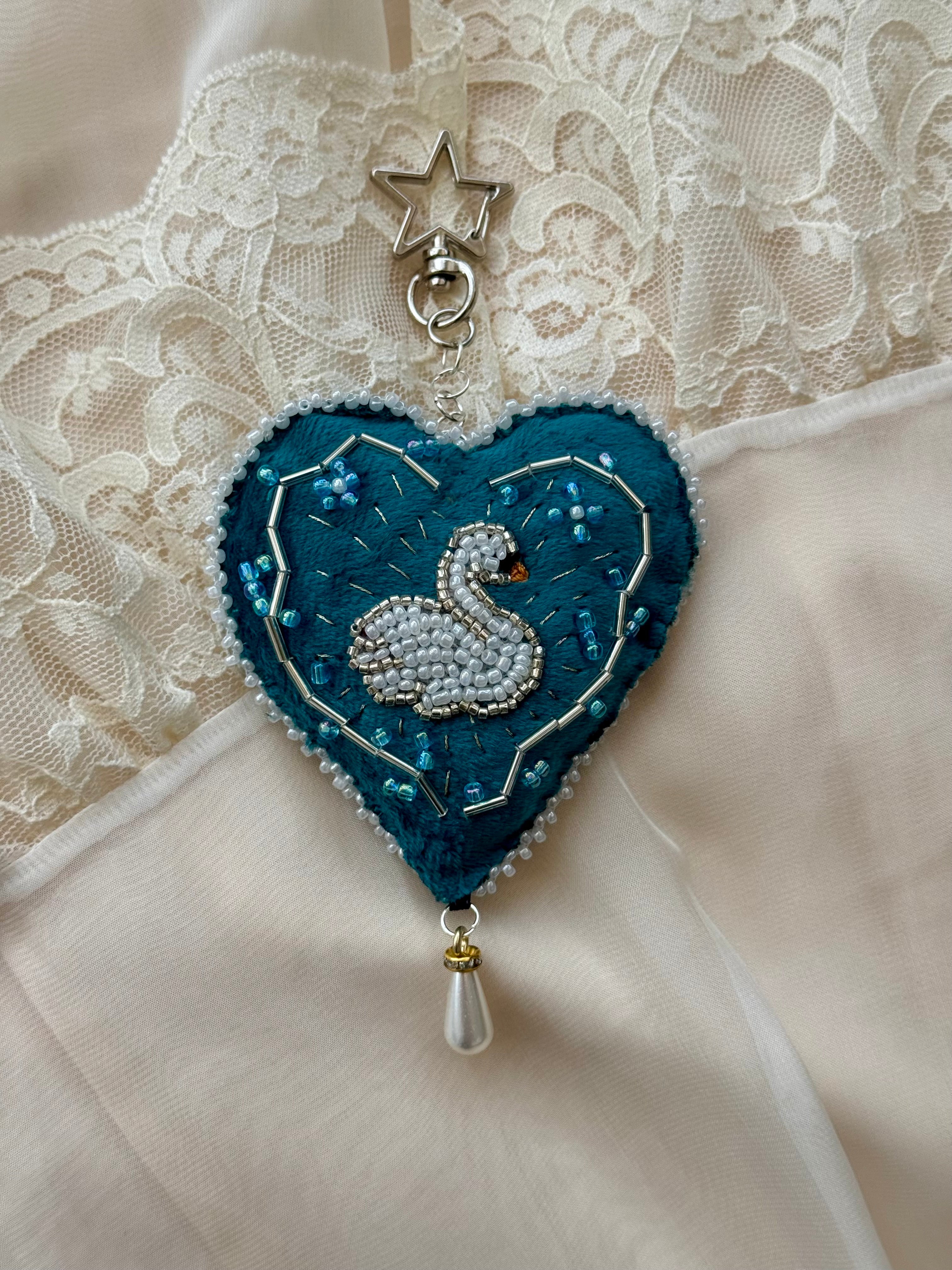 Decorative heart-shaped pendant with a swan design on a lace background