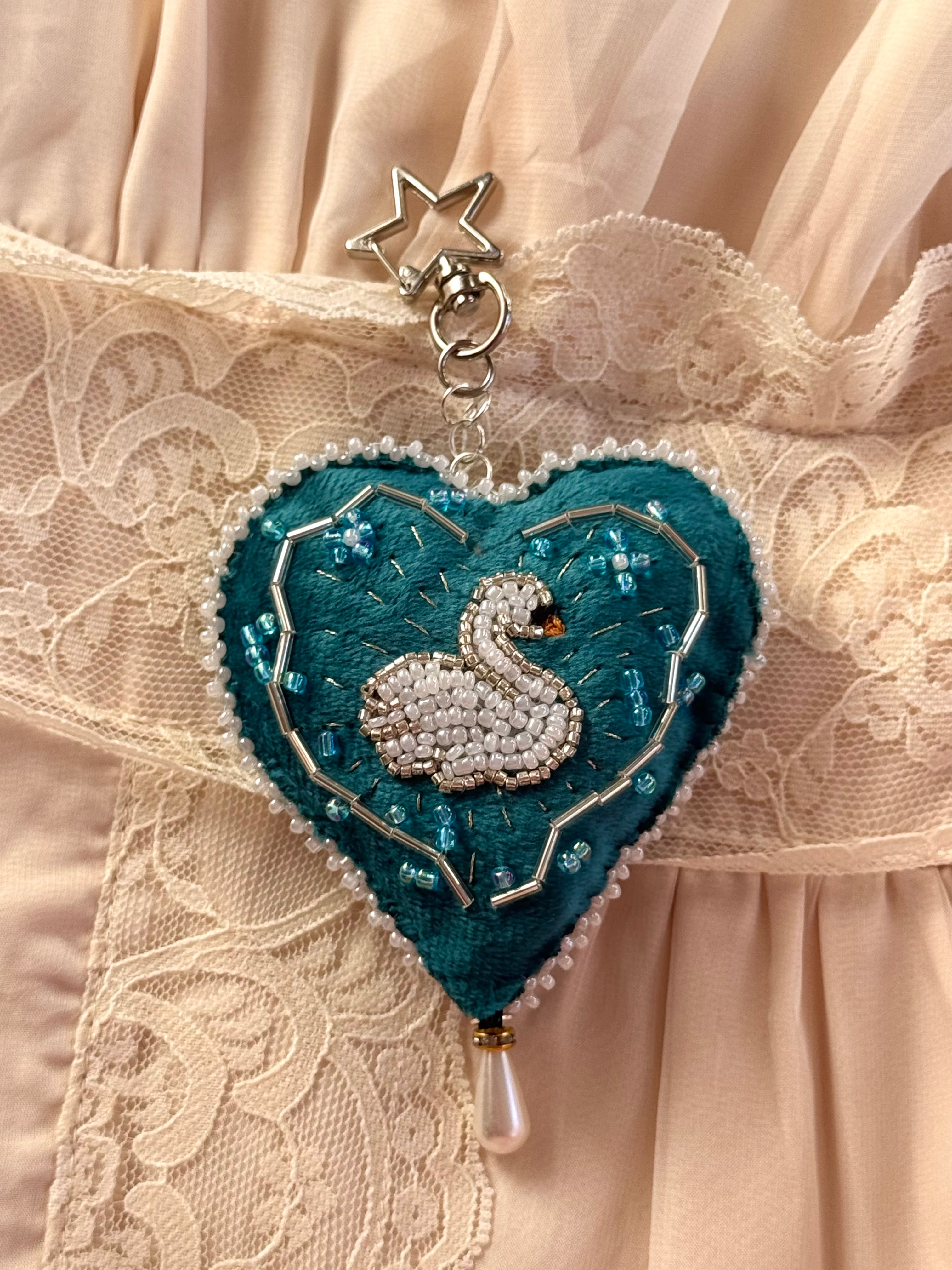Heart-shaped brooch with a swan design on a lace fabric background