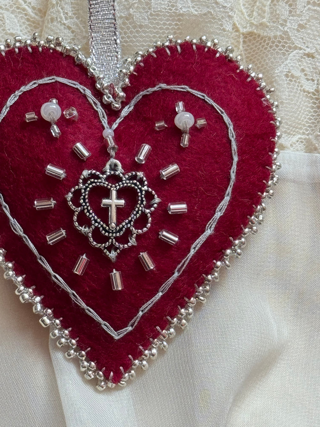 Red heart-shaped embroidered patch with silver thread and beads on a white fabric background