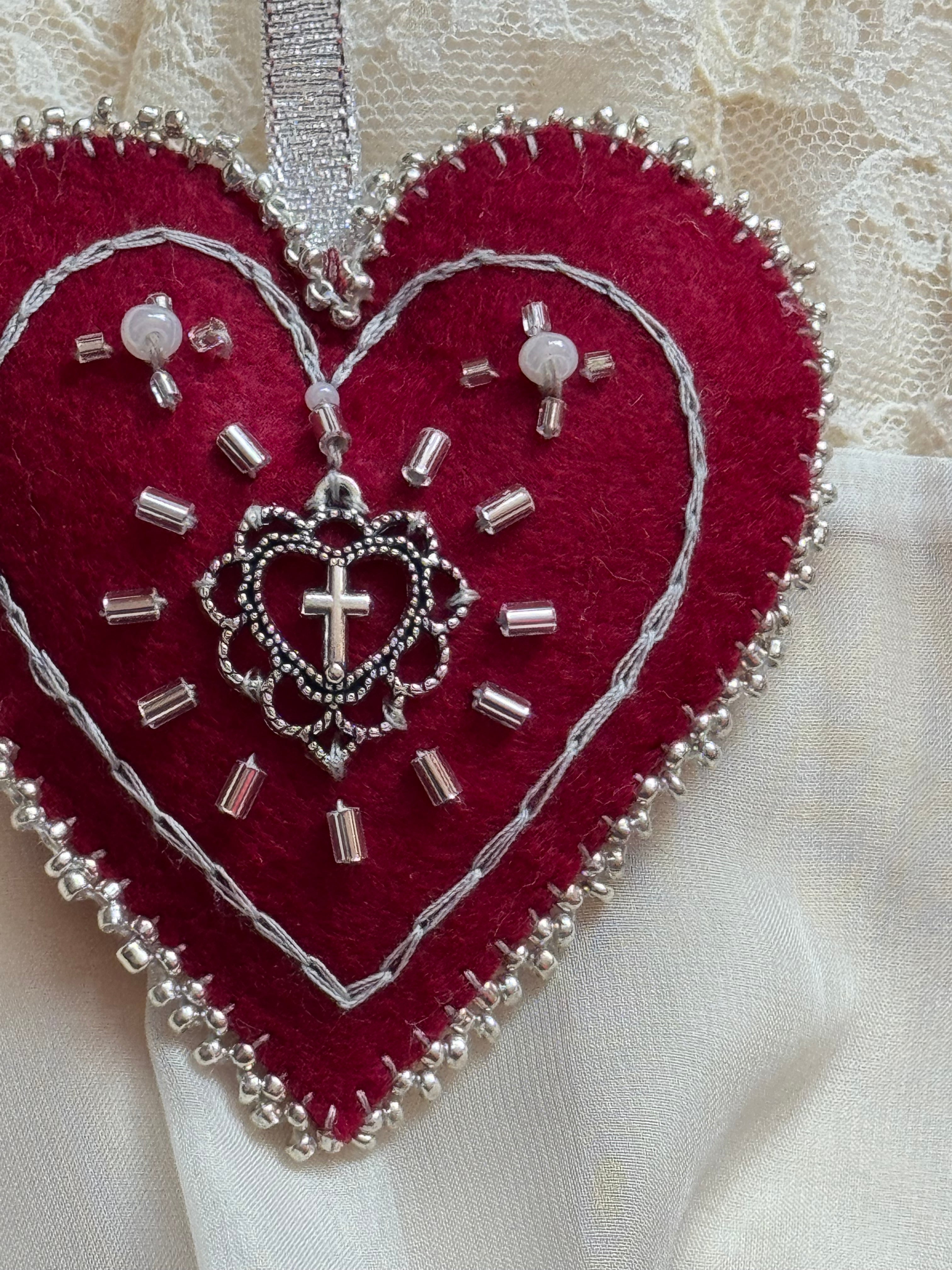 Red heart-shaped embroidered patch with silver thread and beads on a white fabric background