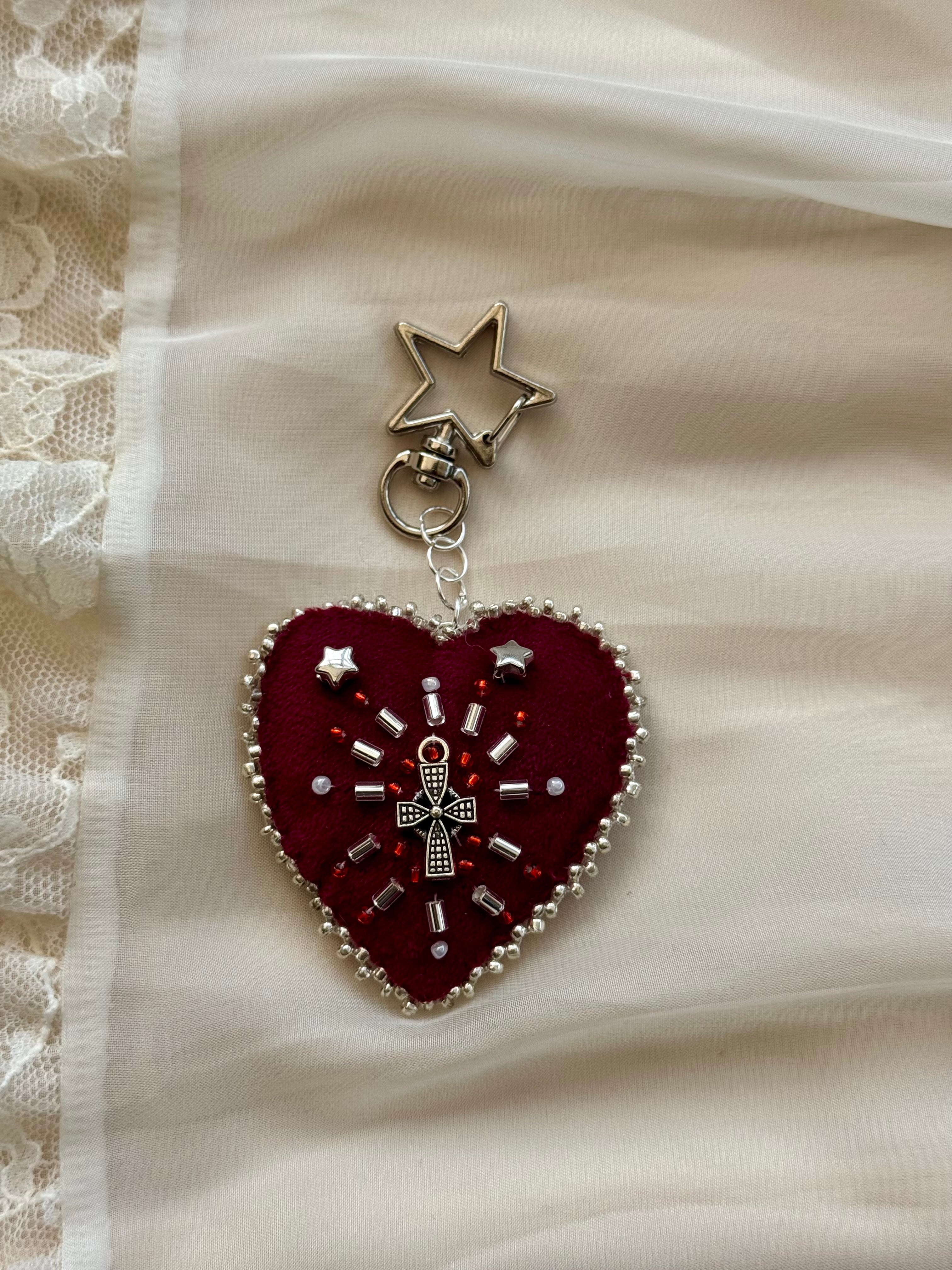 Heart-shaped embroidered pendant keychain with star and cross designs on a lace background