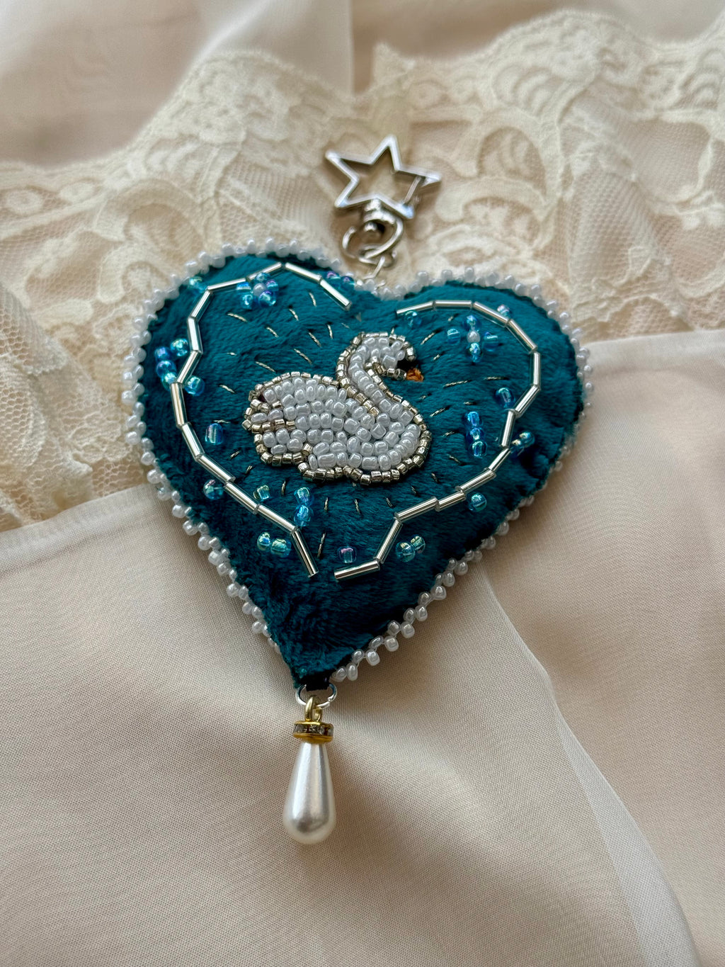 Decorative heart-shaped brooch with a swan design on a lace background