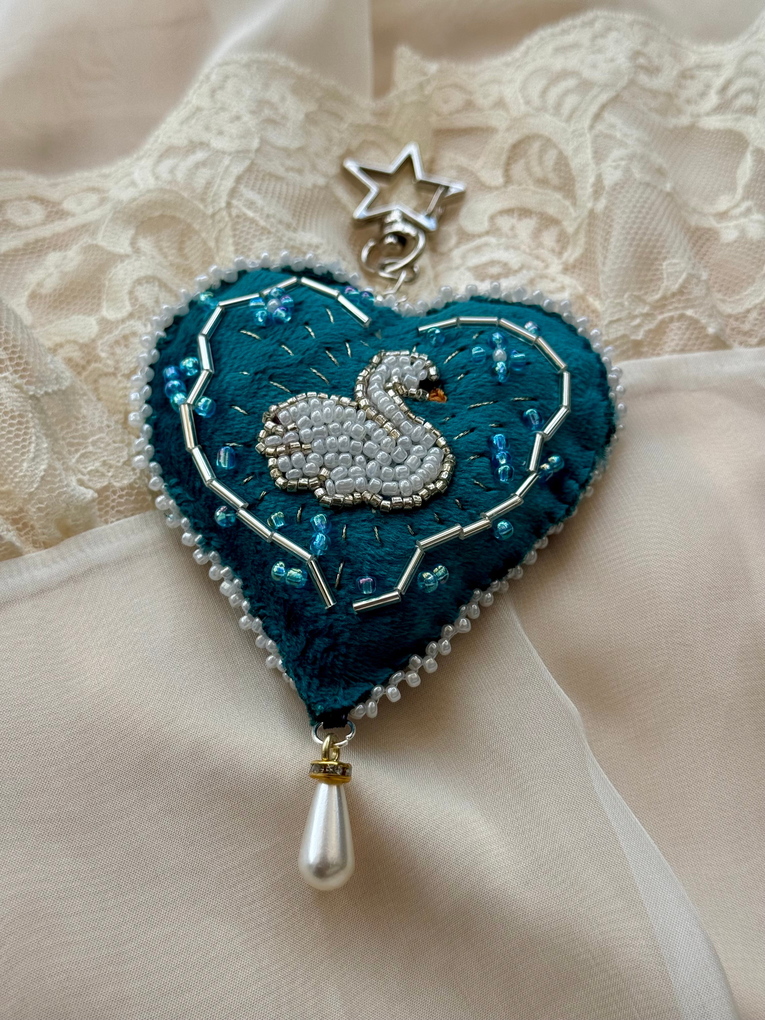 Decorative heart-shaped brooch with a swan design on a lace background