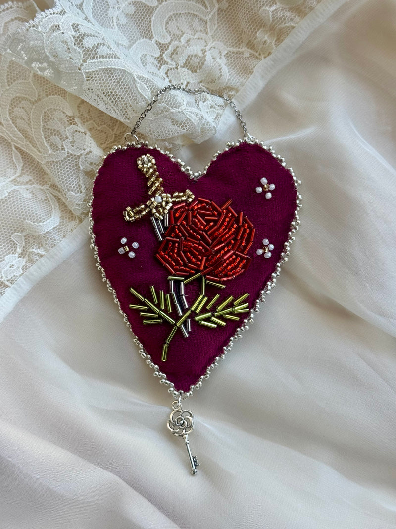 Embroidered heart-shaped decoration with a rose and key on a white lace background