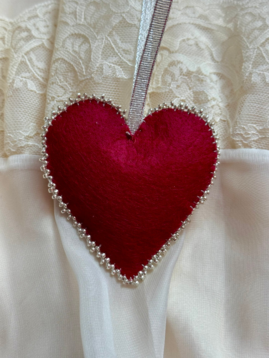 Red heart-shaped fabric ornament with beads on a lace background