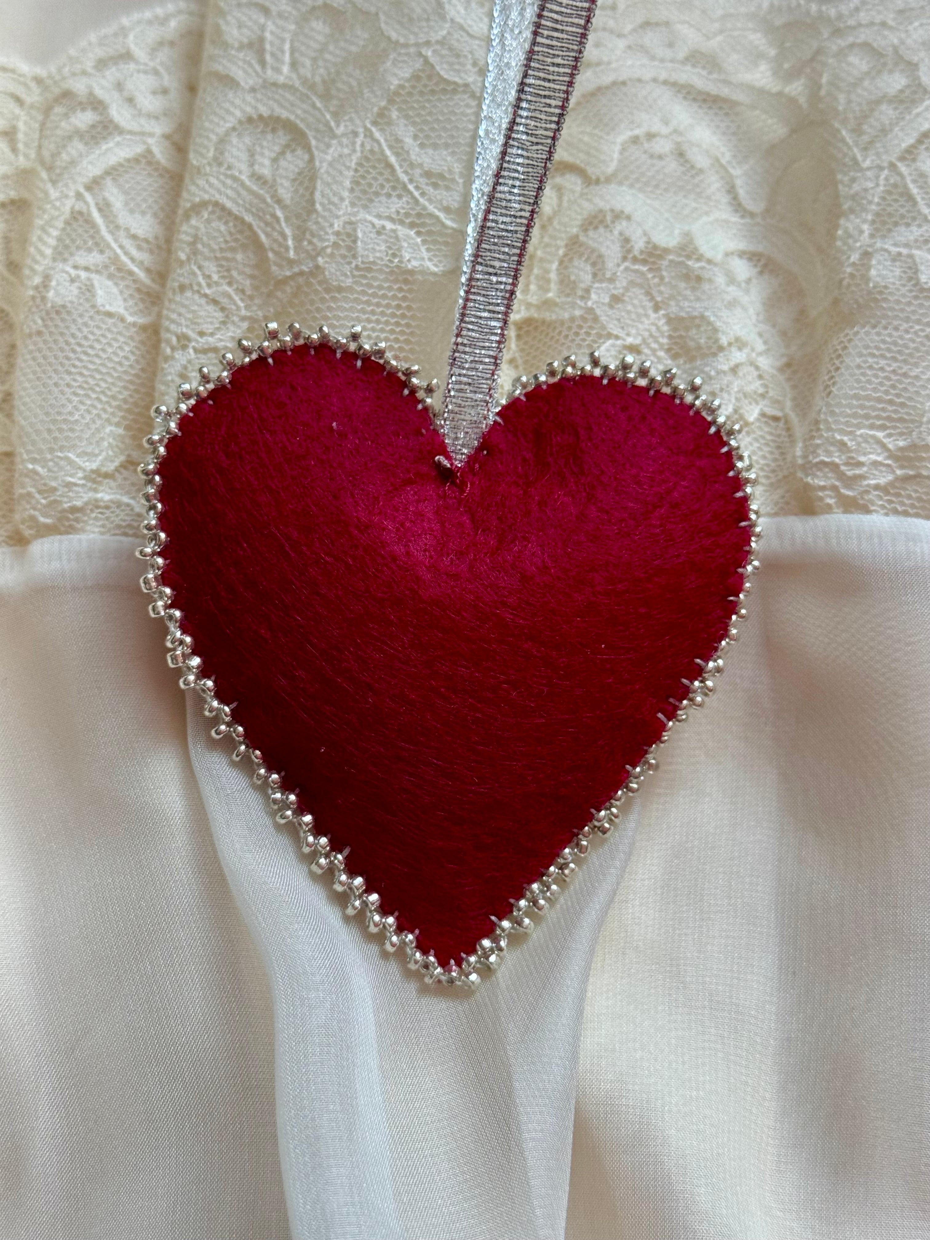 Red heart-shaped fabric ornament with beads on a lace background