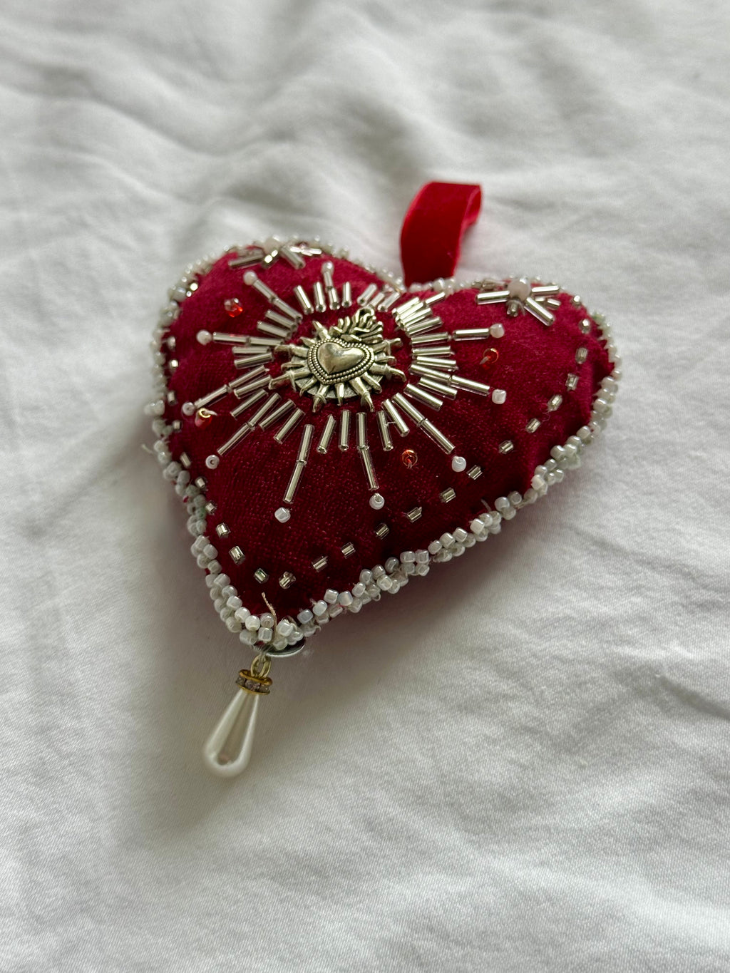 Decorative heart-shaped pillow with beadwork on a white surface