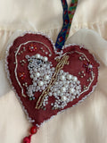 Heart-shaped ornament with beadwork shaping a sacred lamb on a white background with cross