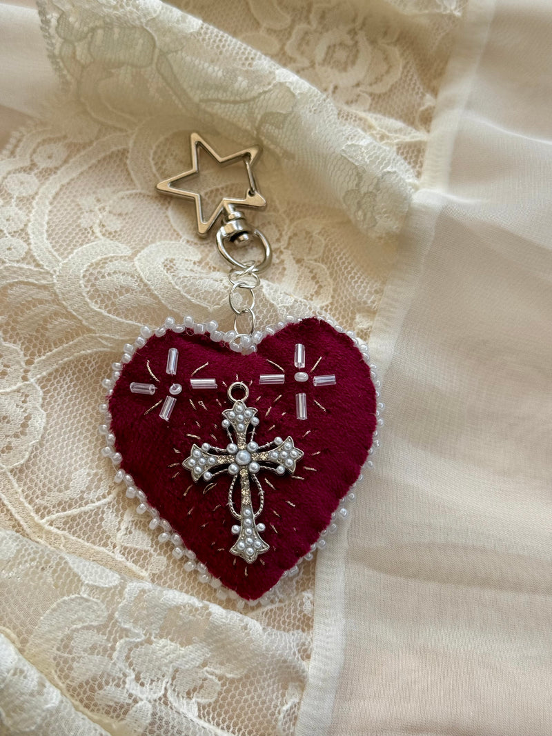 Heart-shaped embroidered pendant keychain with star and cross designs on a lace background