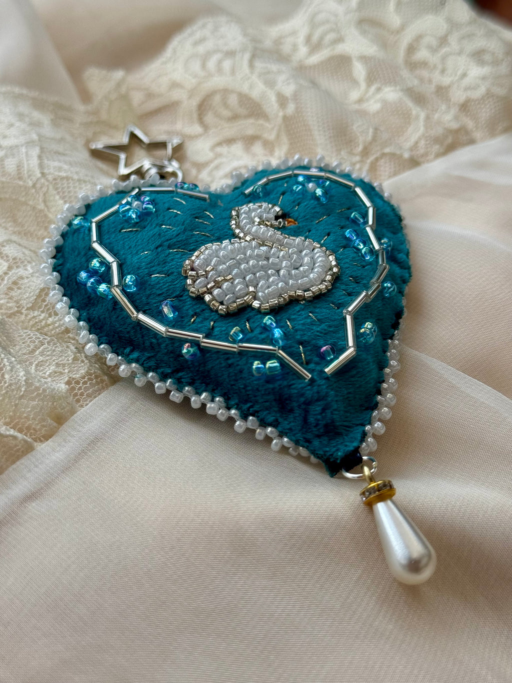 Heart-shaped brooch with a swan design on a textured fabric background