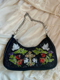 Black handbag with floral and cross embroidery on a beige fabric background