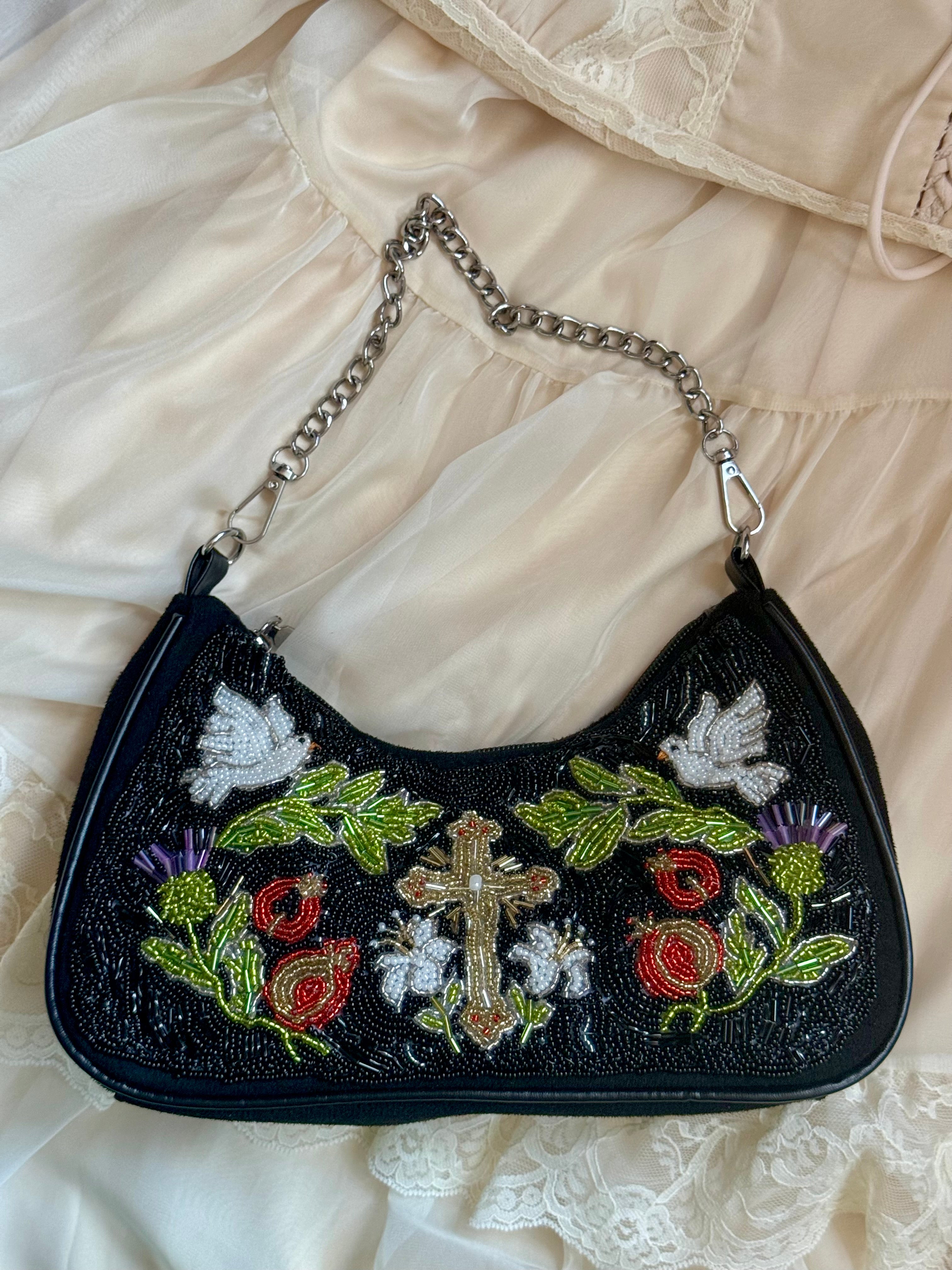 Black handbag with floral and cross embroidery on a beige fabric background