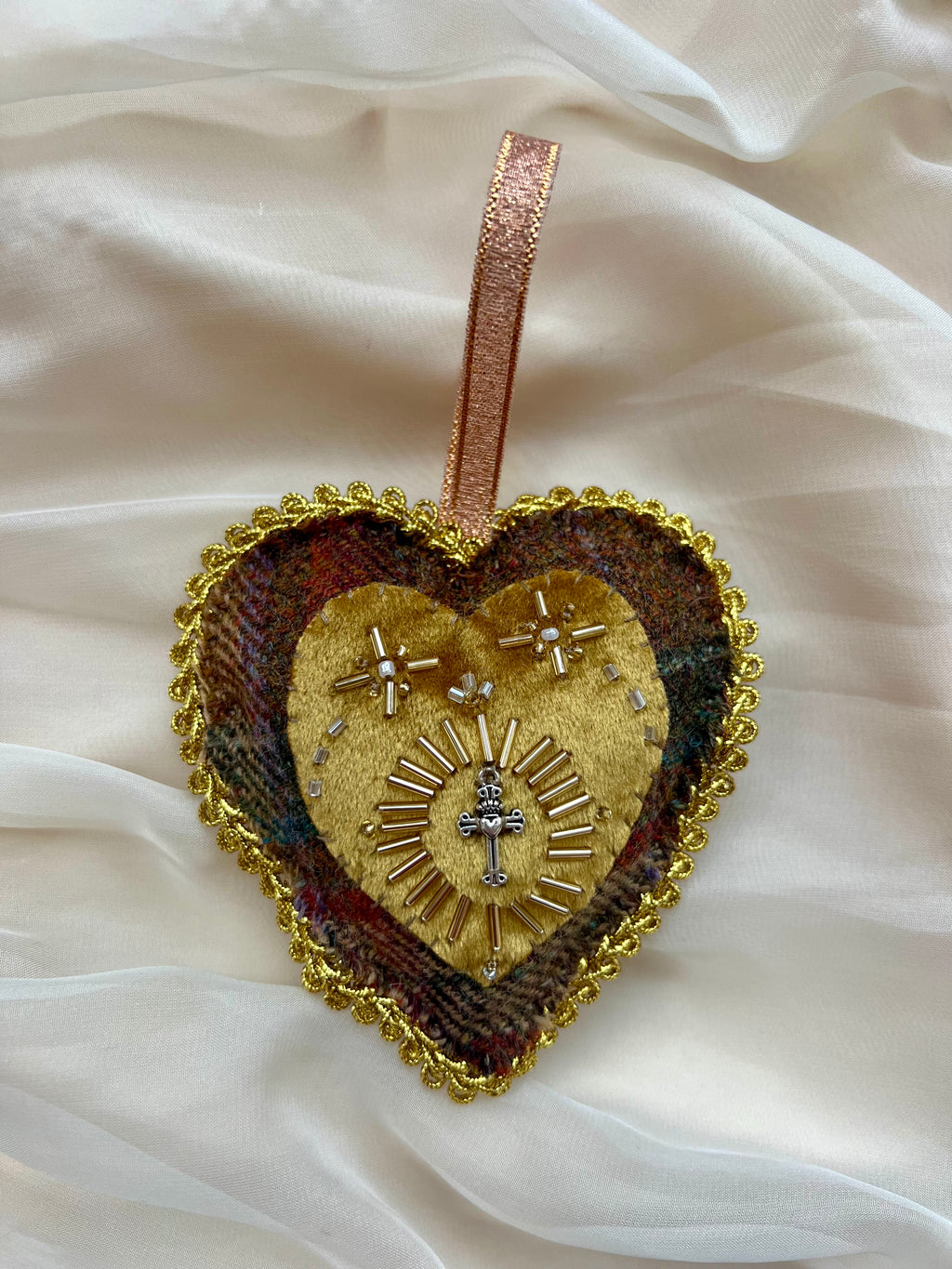 Decorative heart-shaped ornament with gold detailing on a white fabric background