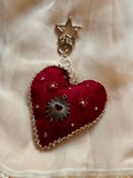 Heart-shaped keychain with star and sun design on a beige fabric background