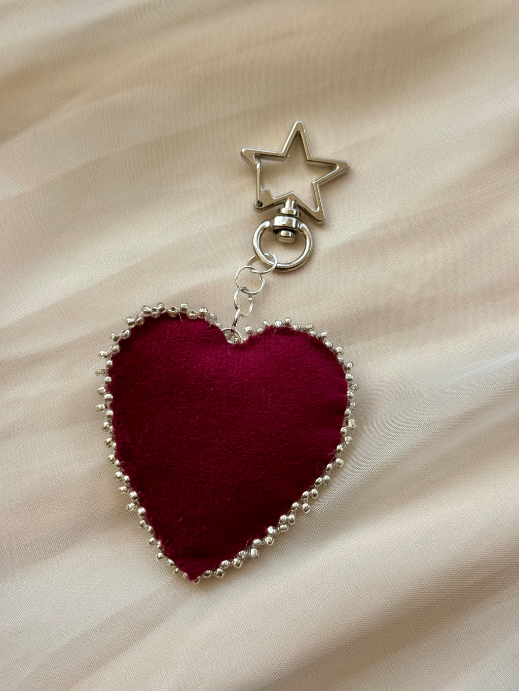 Heart-shaped keychain with star charm on a beige fabric background
