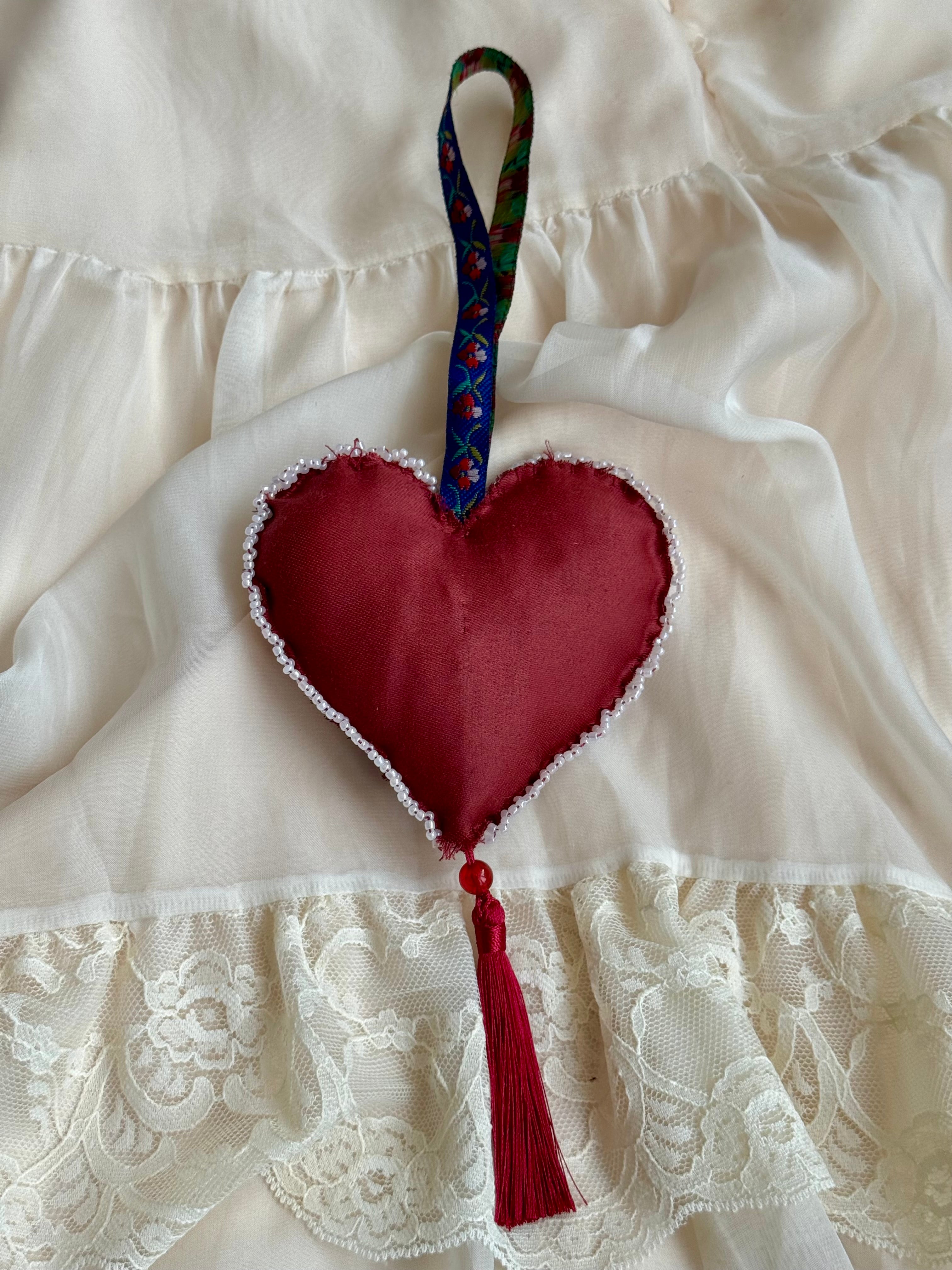 Red heart-shaped fabric ornament with tassel on a white lace background