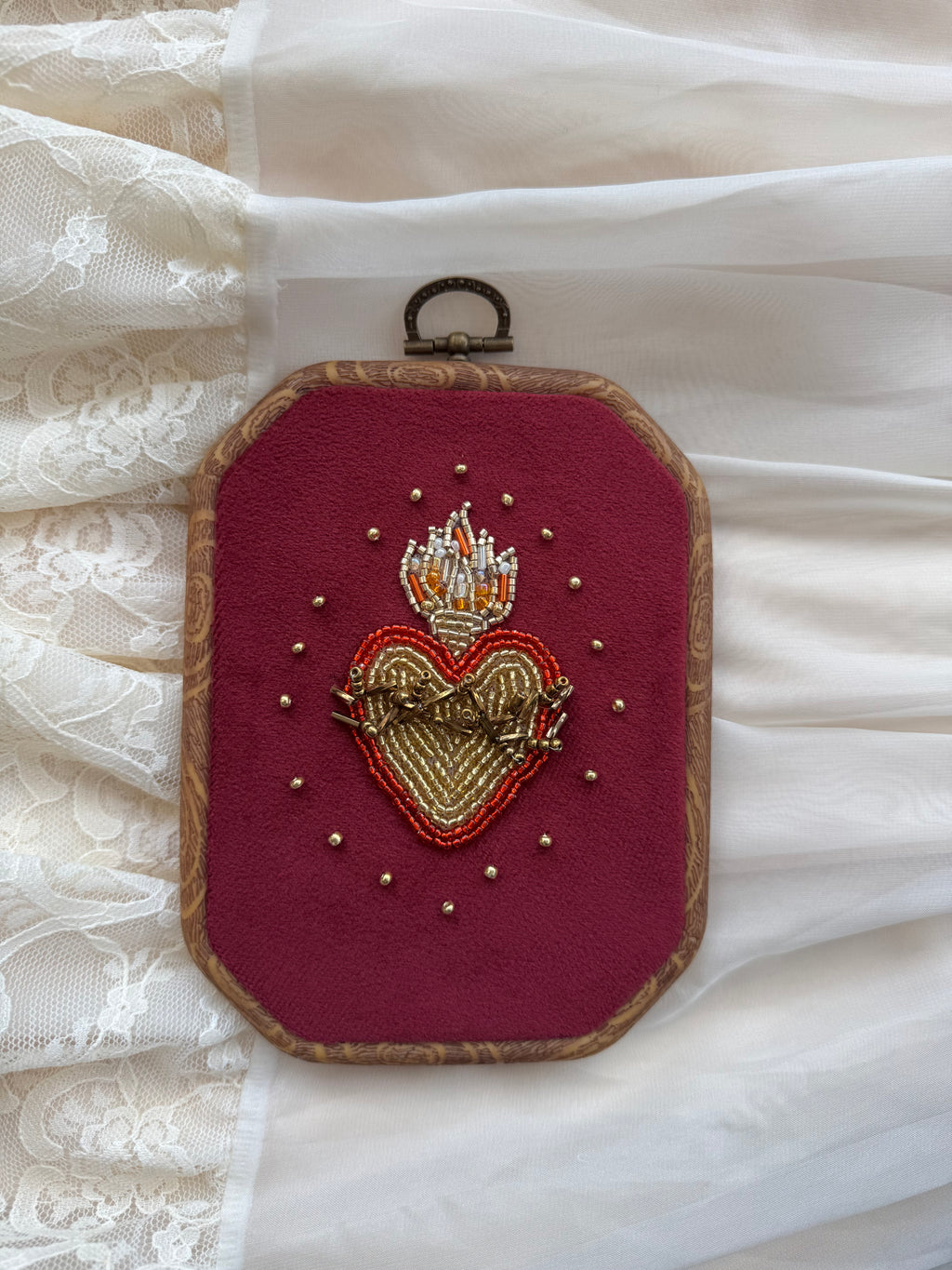  Embroidered wall hanging with a sacred heart design on velvet, framed in a wood-look frame with metal hanging, on a white fabric surface.