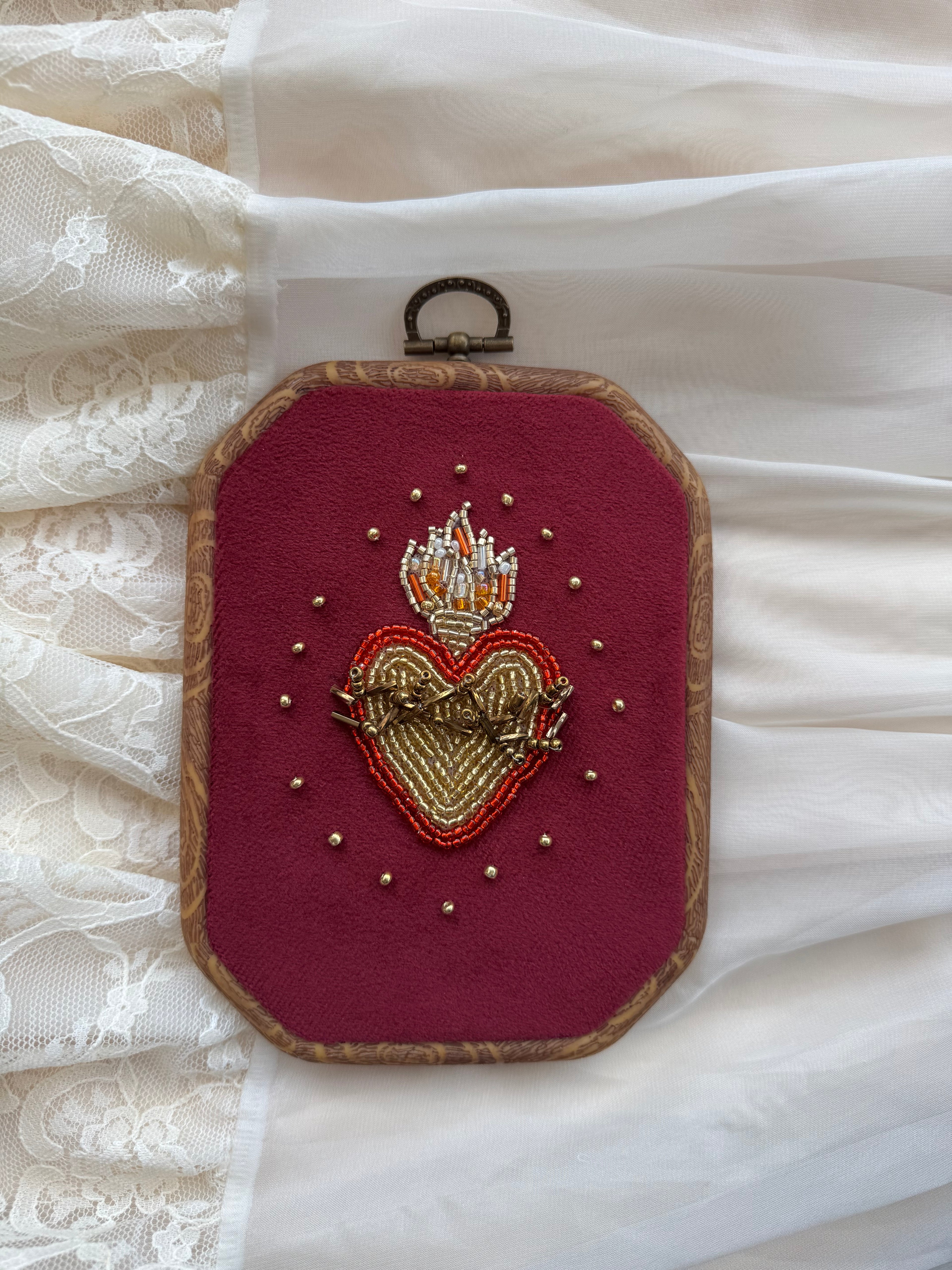  Embroidered wall hanging with a sacred heart design on velvet, framed in a wood-look frame with metal hanging, on a white fabric surface.