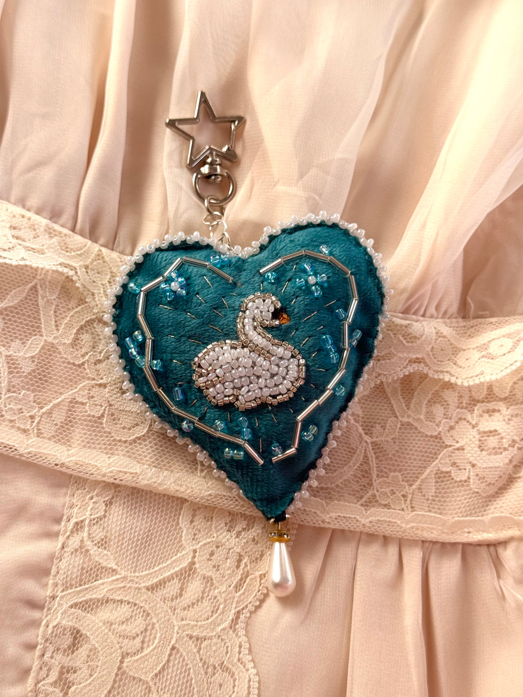 Heart-shaped keychain with a swan design on a lace fabric background