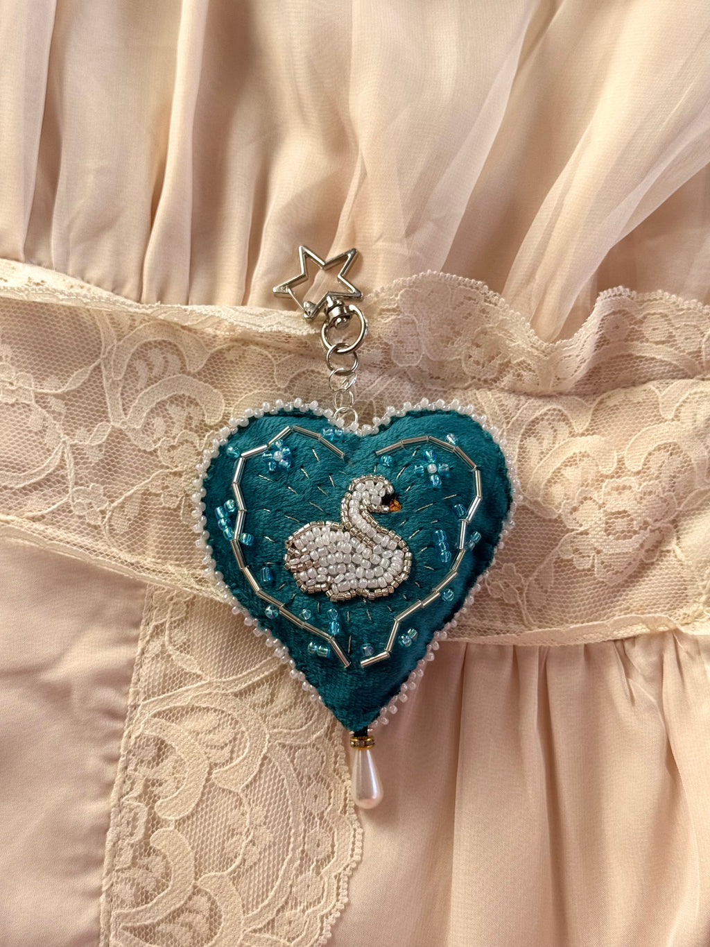 Heart-shaped brooch with a swan design on a lace fabric background