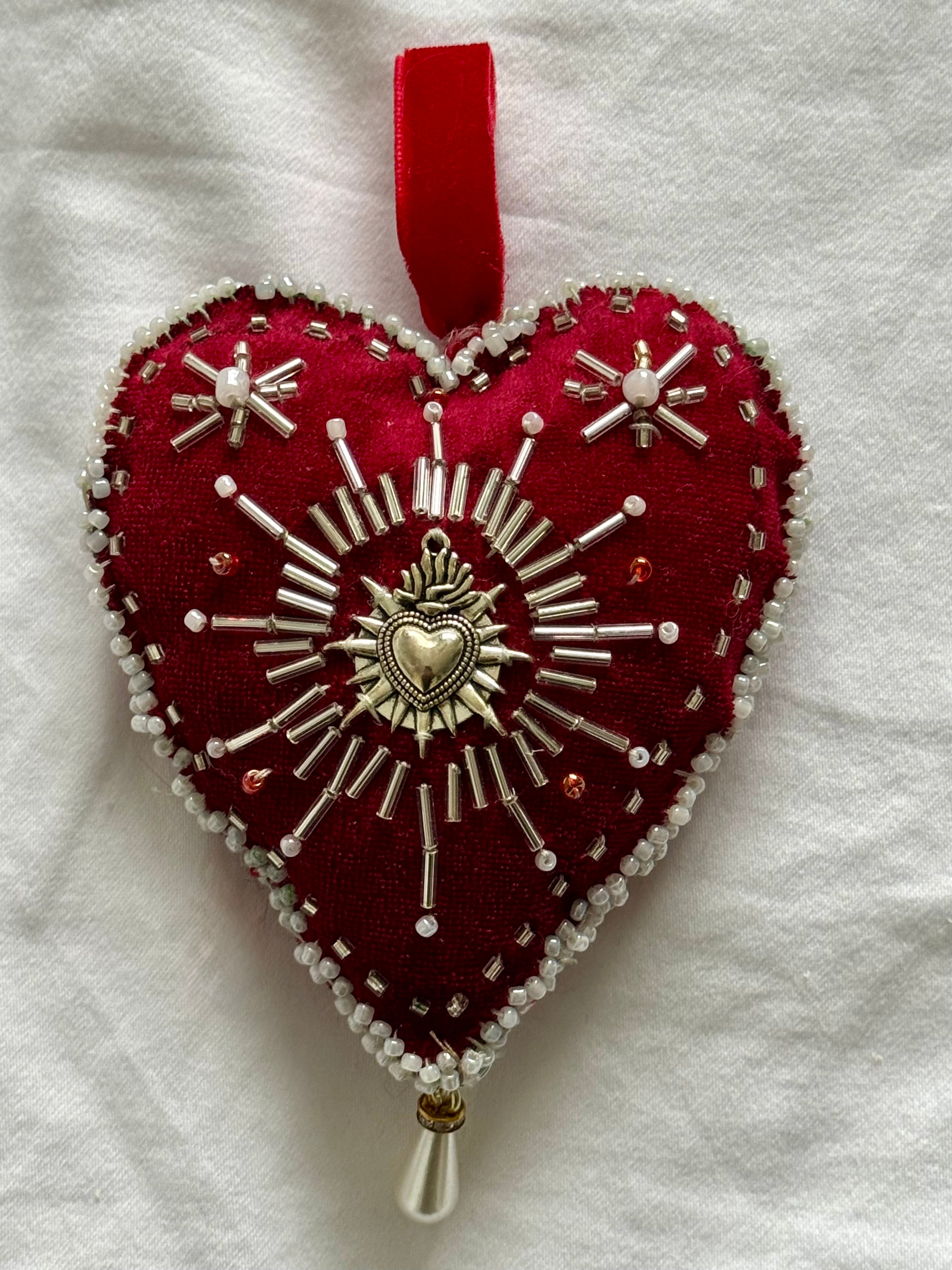 Decorative heart ornament with red fabric and silver embroidery on a white background