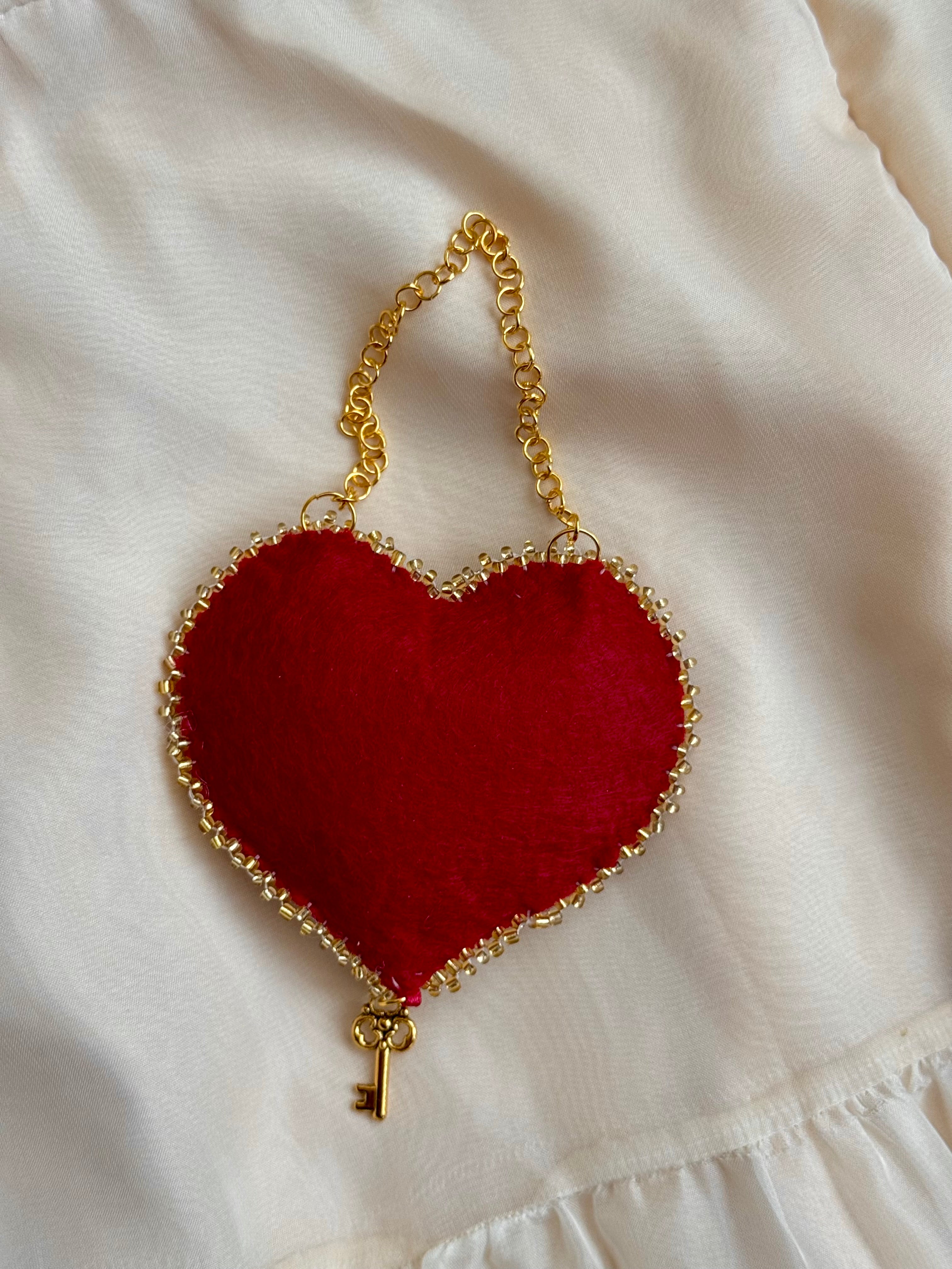 Red heart-shaped bag with a gold chain and key charm on a white background
