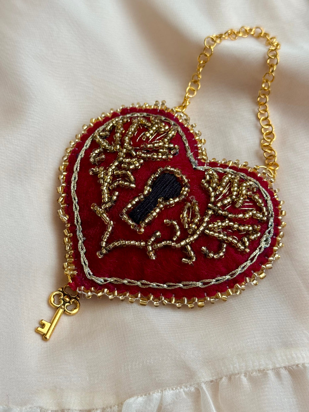 Heart-shaped embroidered pendant with key design on a white fabric background