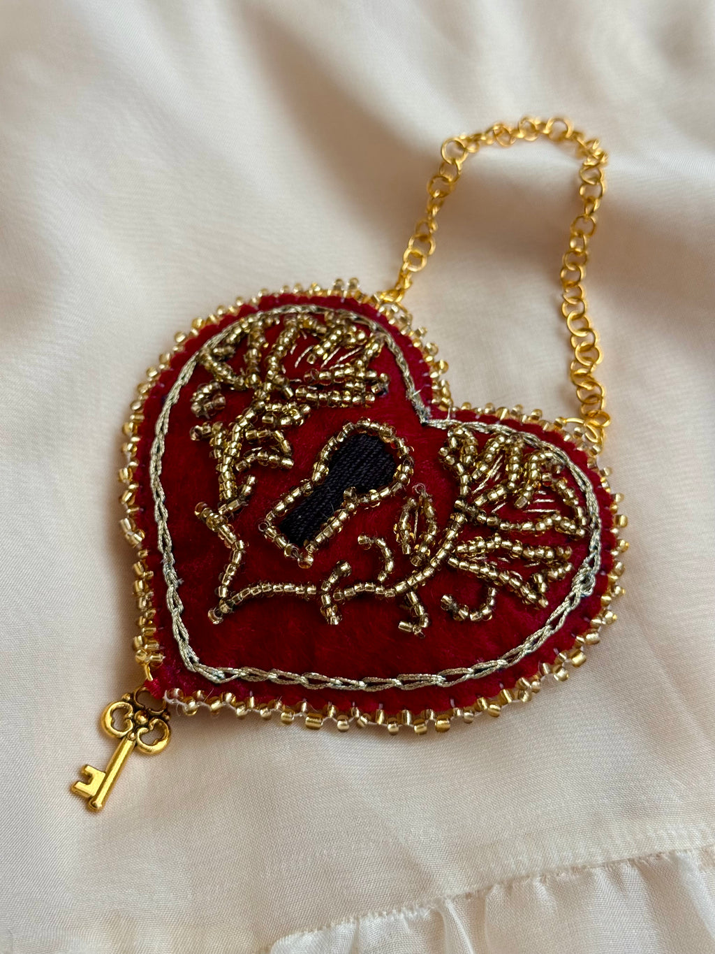 Decorative heart-shaped purse with gold chain and key charm on a white fabric background