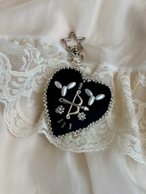 Heart-shaped black pendant with white floral designs and silver accents on a lace background