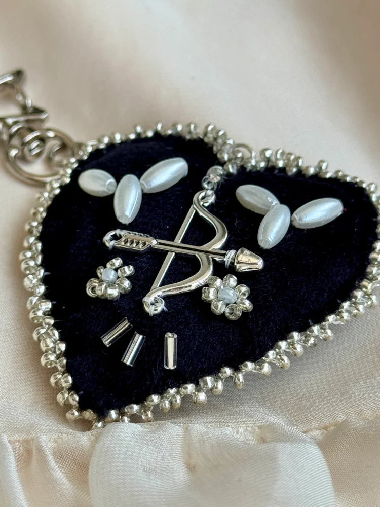 Heart-shaped keychain with bow and arrow design on a soft fabric background