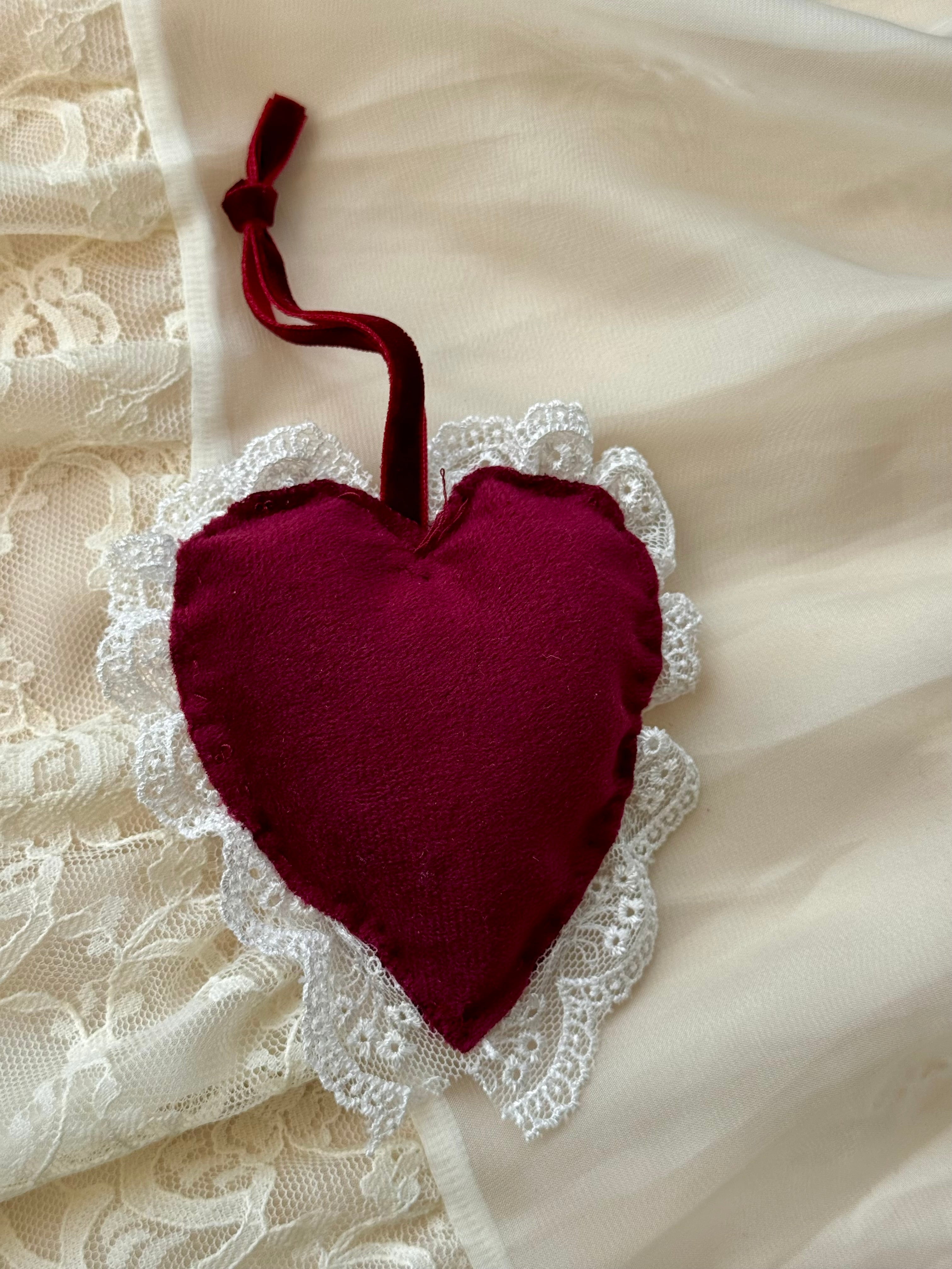 Heart-shaped fabric ornament with lace trim on a textured white background