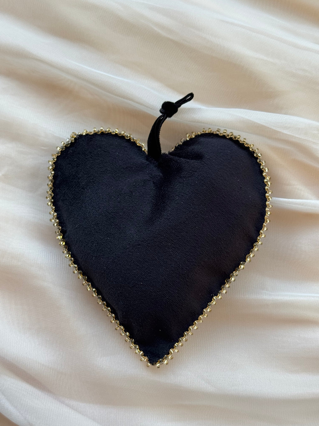 Girdle of Venus black velvet heart-shaped ornament with gold beaded edge on a white fabric background