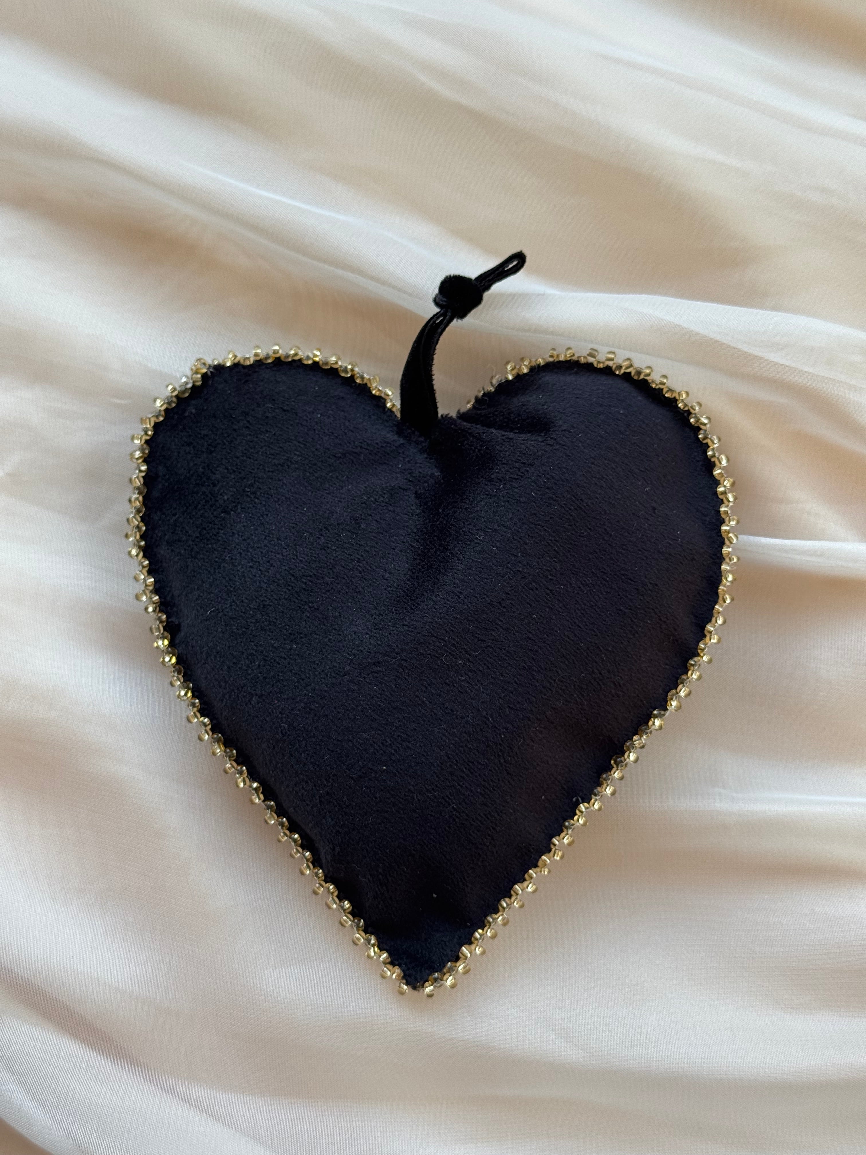 Girdle of Venus black velvet heart-shaped ornament with gold beaded edge on a white fabric background