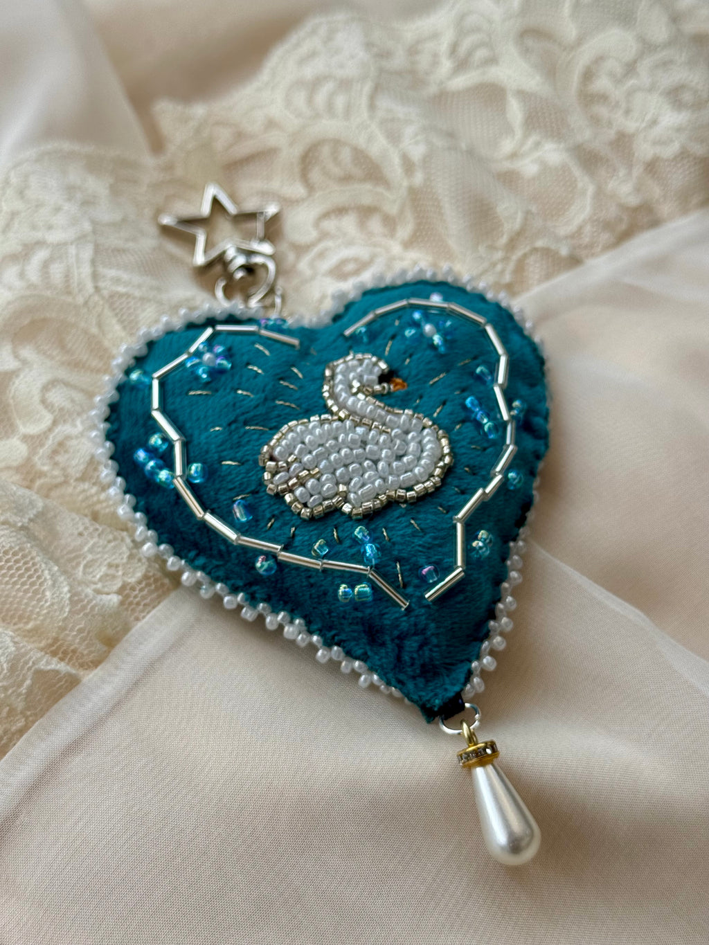 Heart-shaped embroidered pendant with a beaded swan design on a textured fabric background