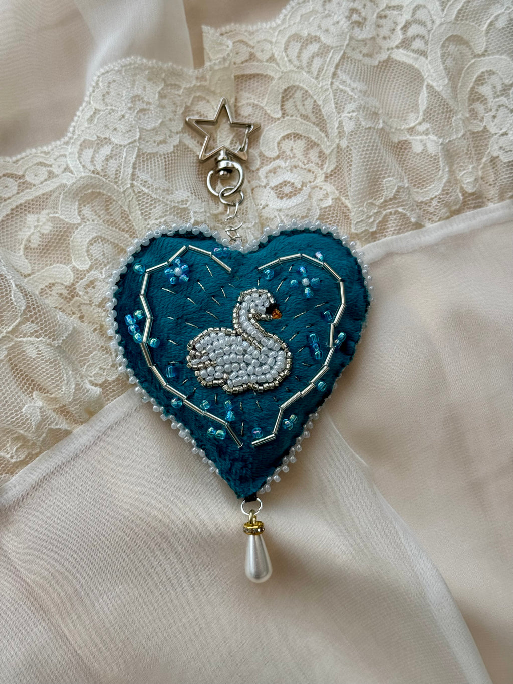 Decorative heart-shaped brooch with a swan design on a lace background