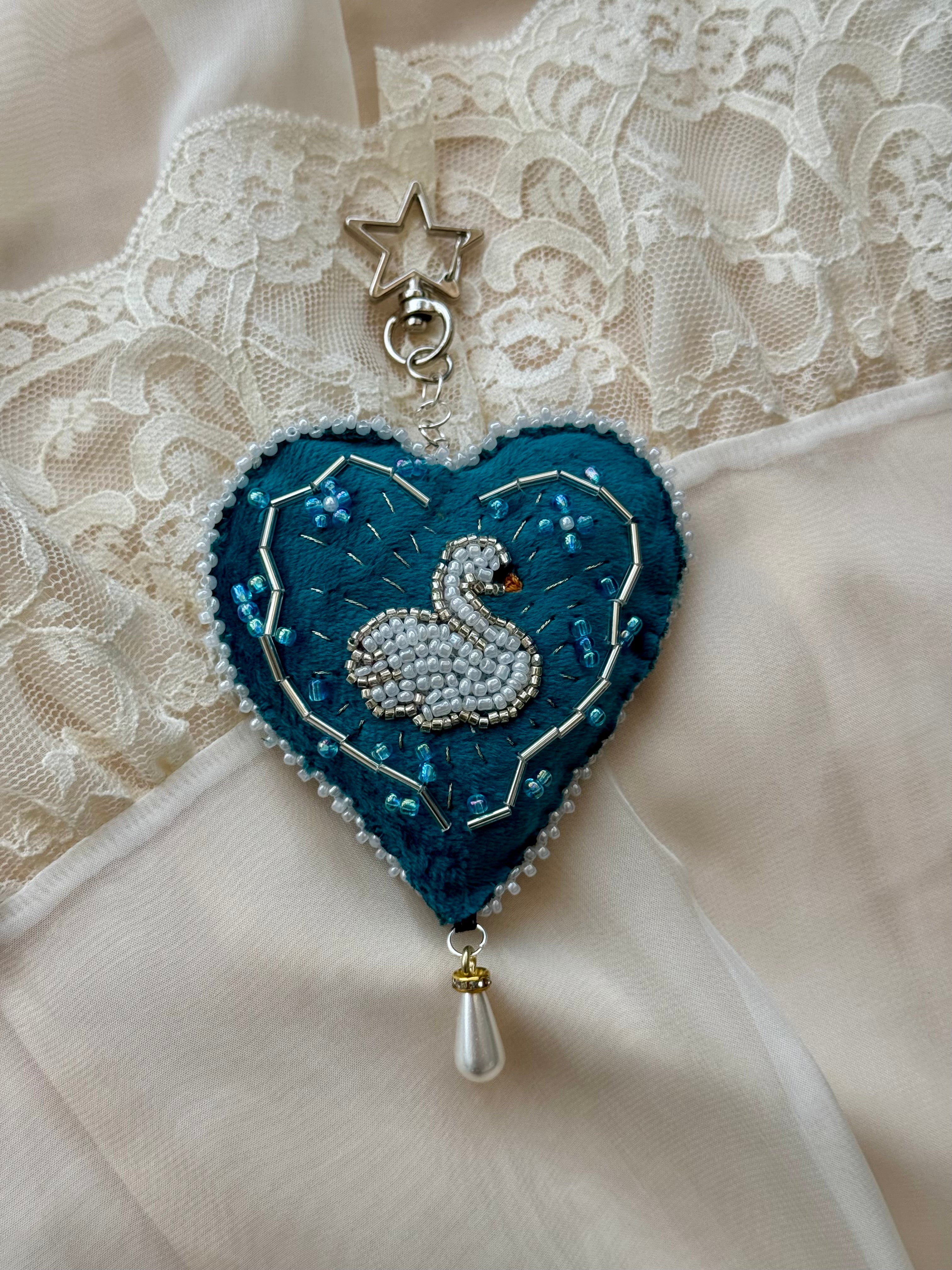 Decorative heart-shaped brooch with a swan design on a lace background